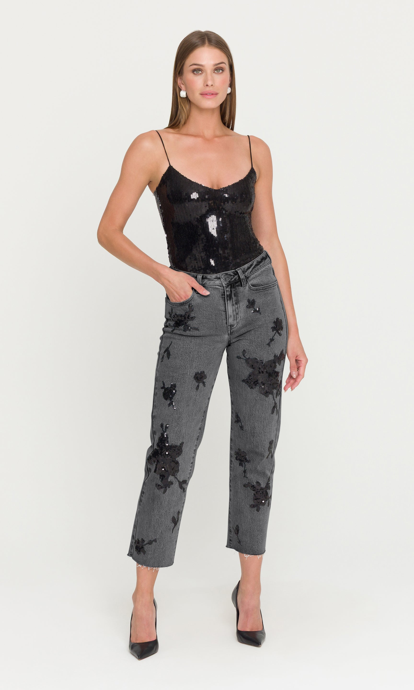 Woman wearing a black sequin top and gray floral-patterned pants on a white background
