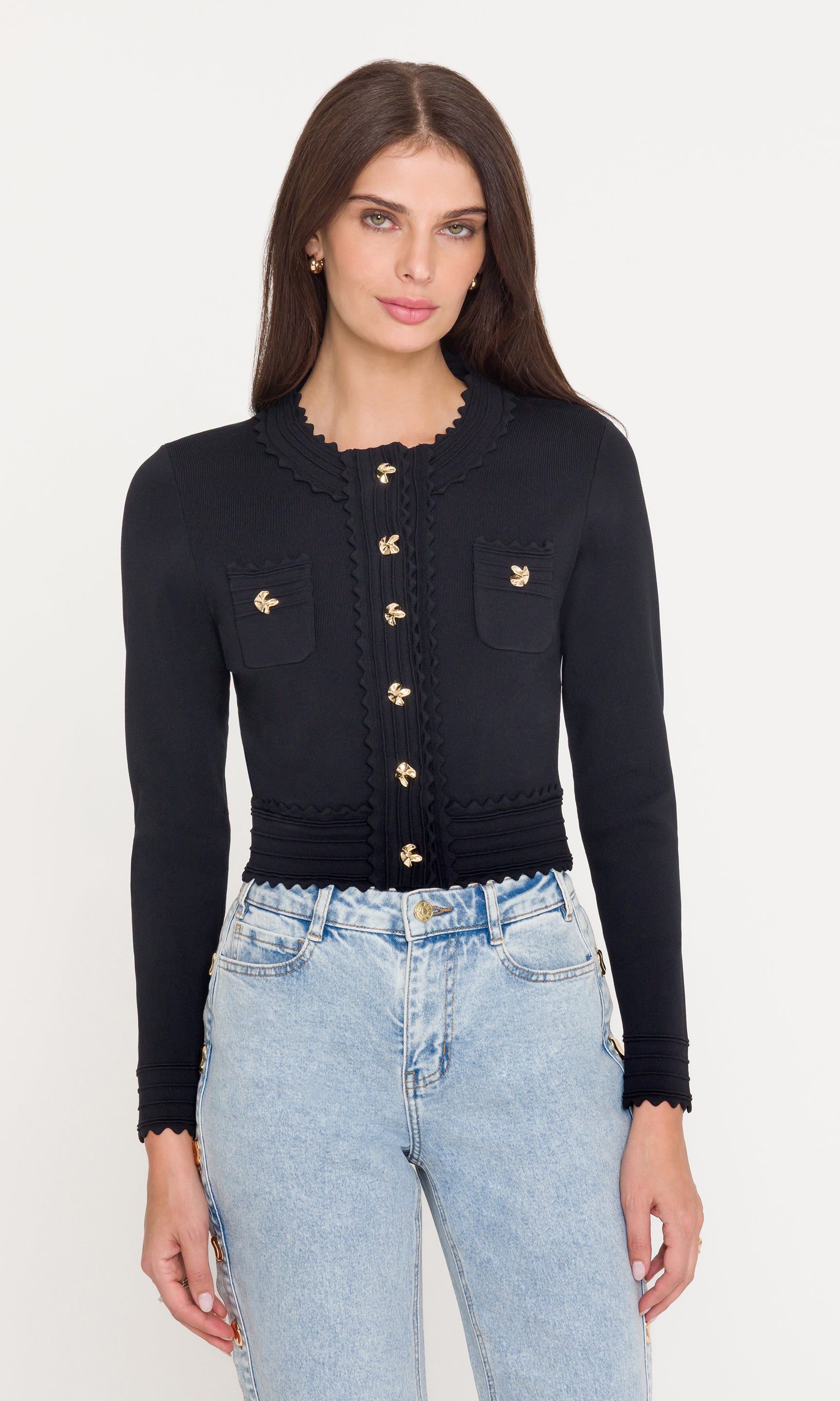 Woman wearing a black cardigan with gold buttons and light blue jeans on a white background