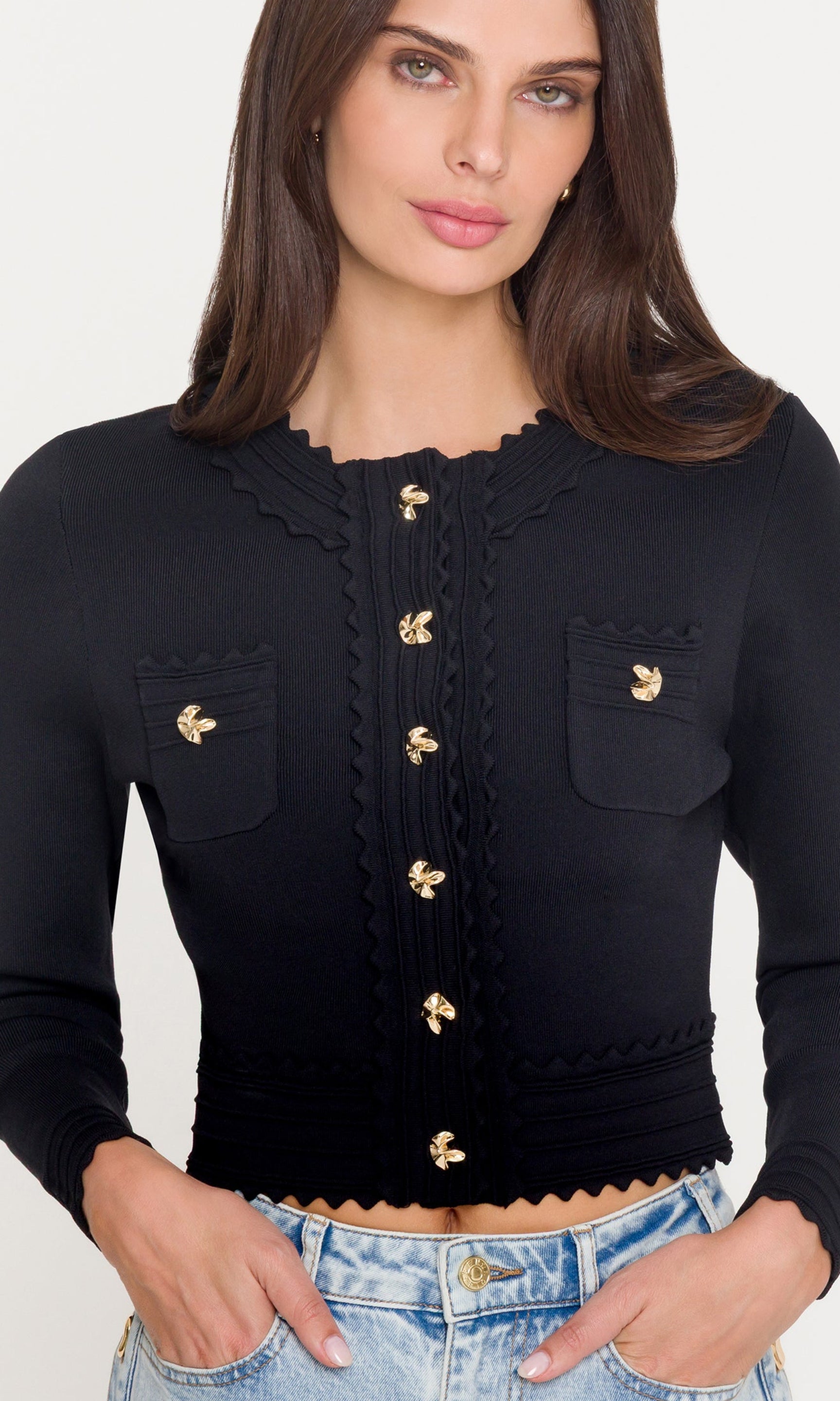 Woman wearing a black cardigan with gold buttons on a white background