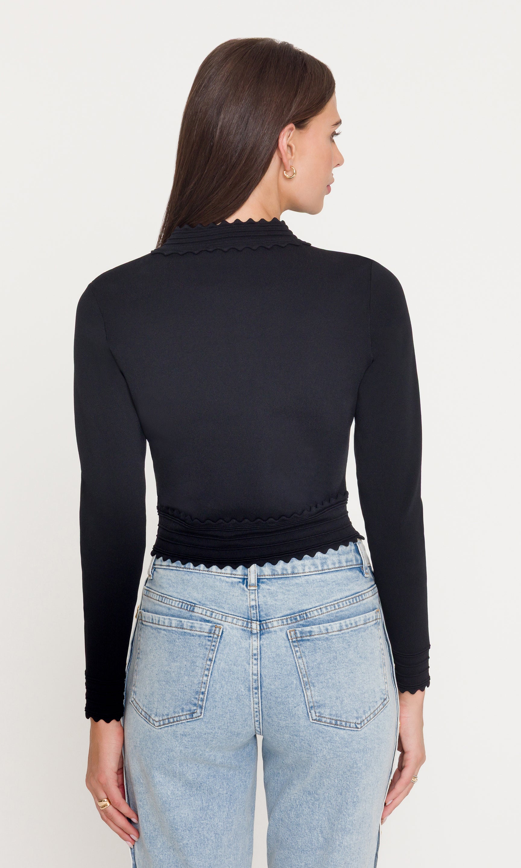 Person wearing a black long-sleeve top and light blue jeans on a white background