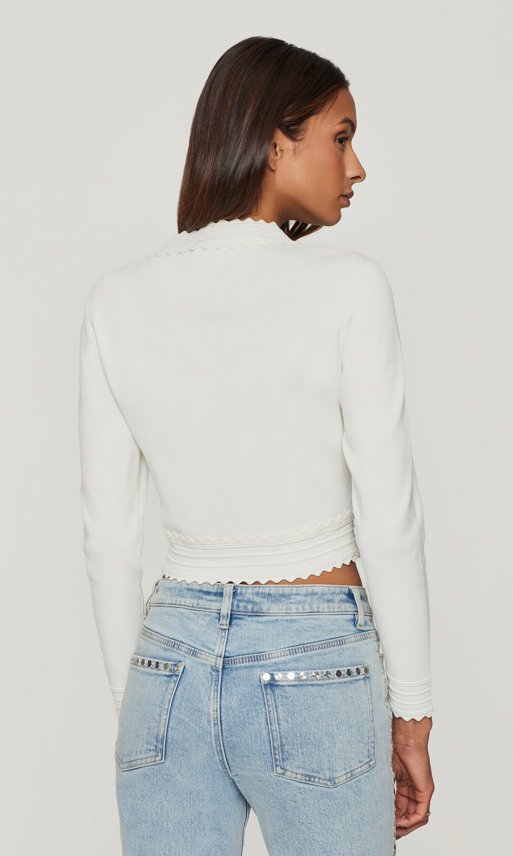 Back view of model wearing a white cardigan and blue jeans on a white background