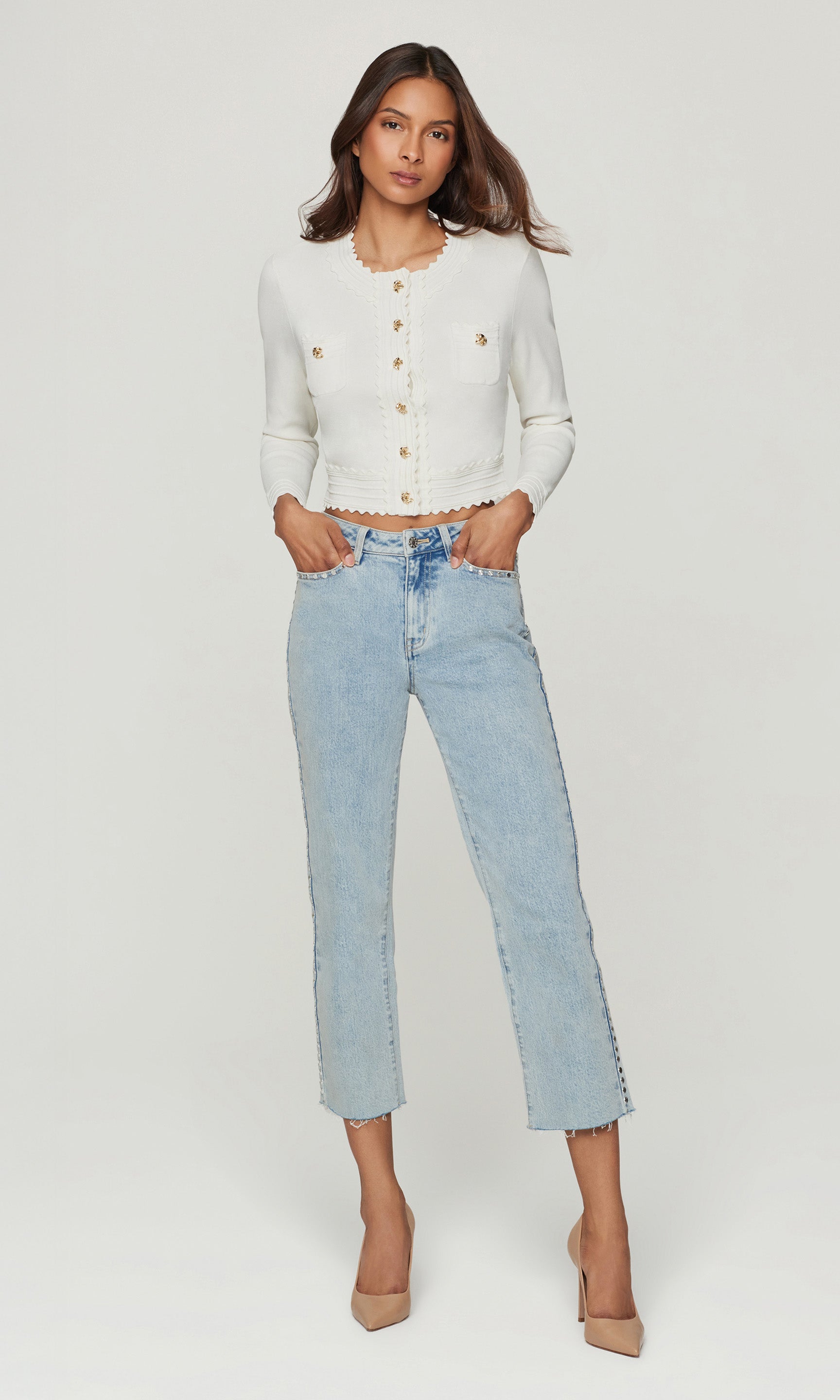 Full body image of model wearing a white cardigan with gold buttons and blue jeans on a white background