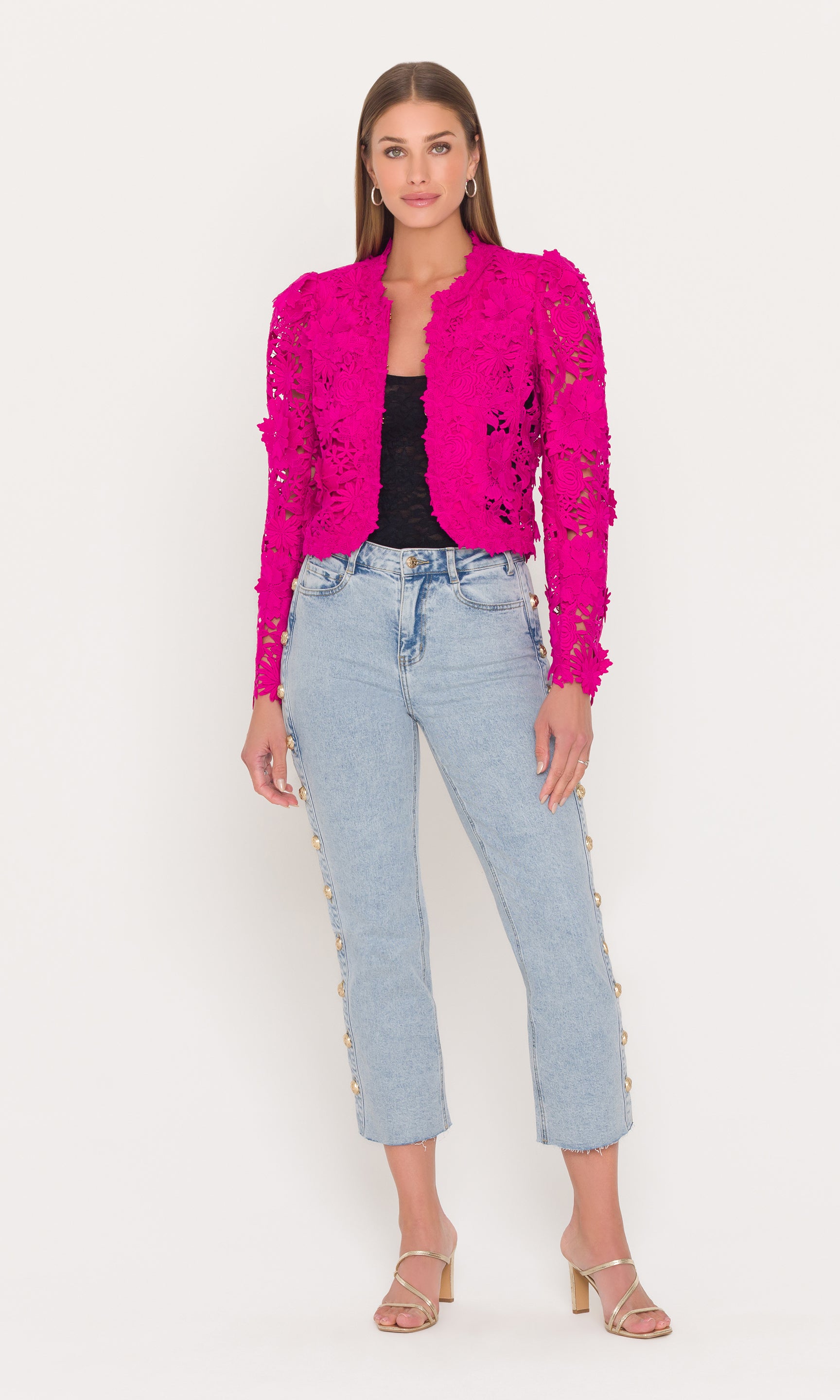 Full body image of woman wearing a bright pink jacket with floral embroidery and light blue jeans on a white background