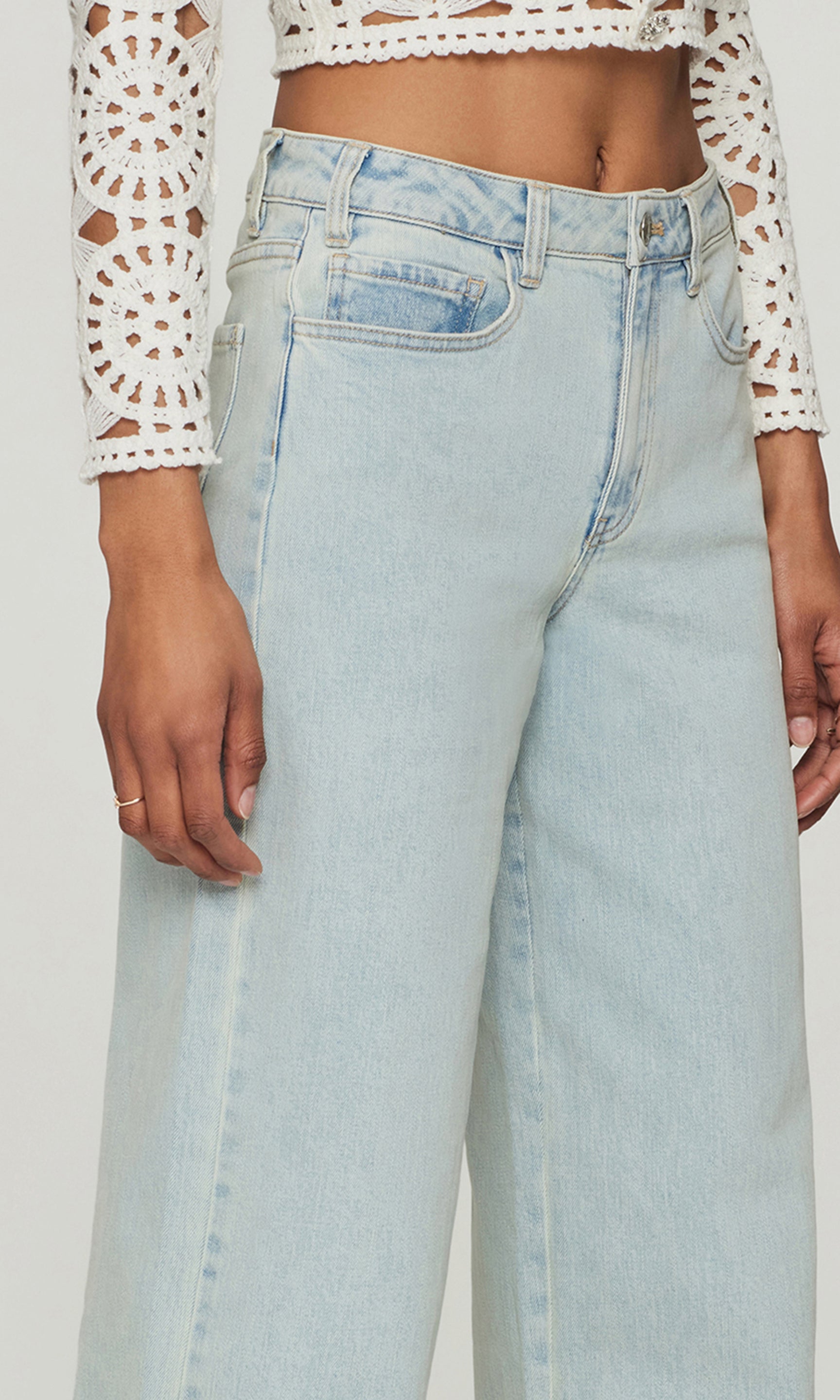 Close-up of light blue jeans worn with a white lace top on a plain background