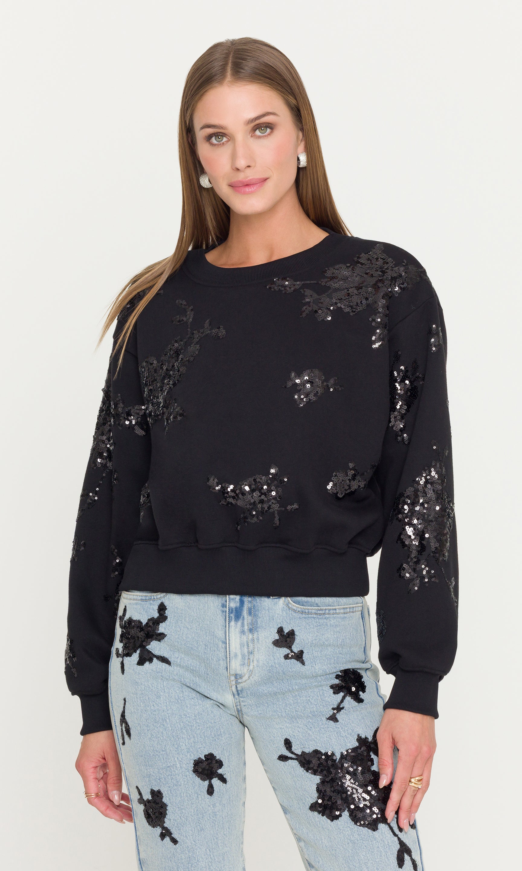 Woman wearing a black sweatshirt with sequin embellishments on a white background