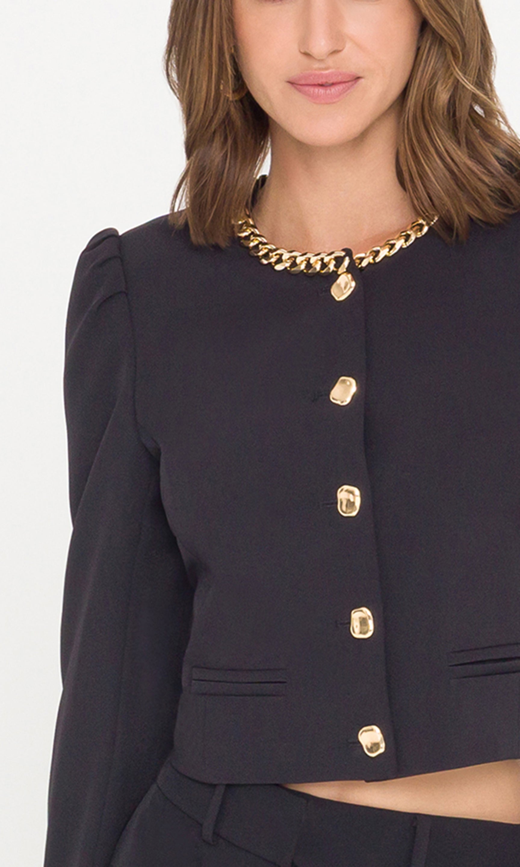 Detail crop image of model wearing a black cropped jacket with a gold chain neckline and gold buttons