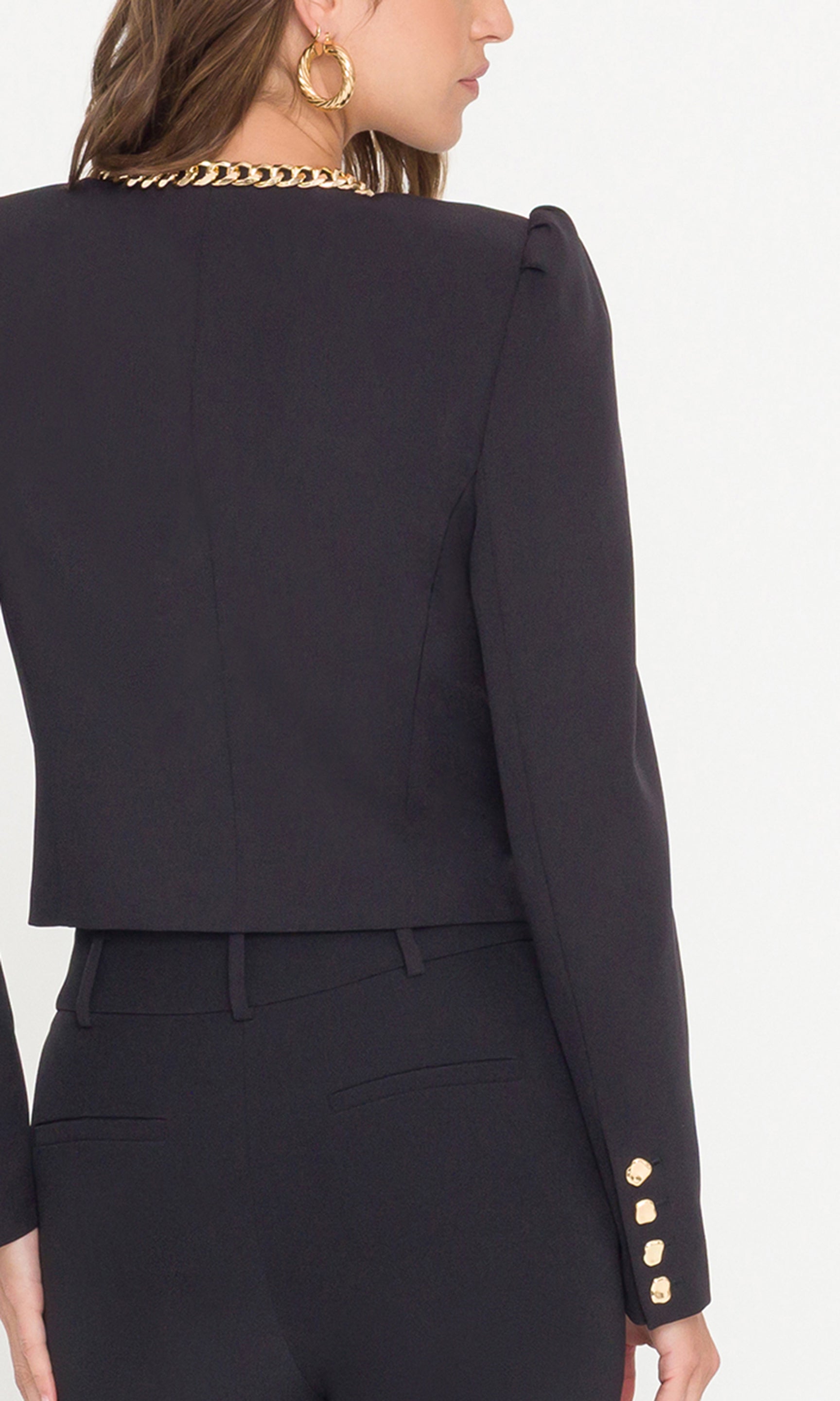 Black blazer with gold buttons worn by a person on a white background