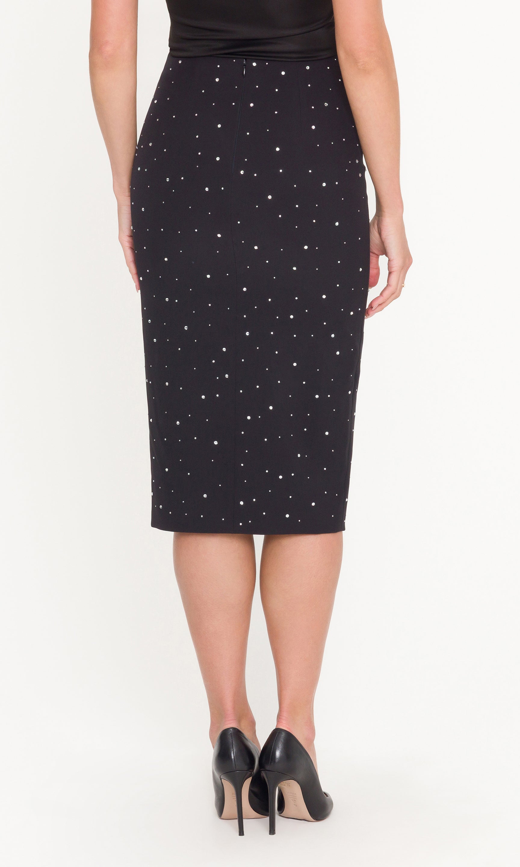 Back view of black pencil skirt with scattered crystal embellishments worn by a person on a white background