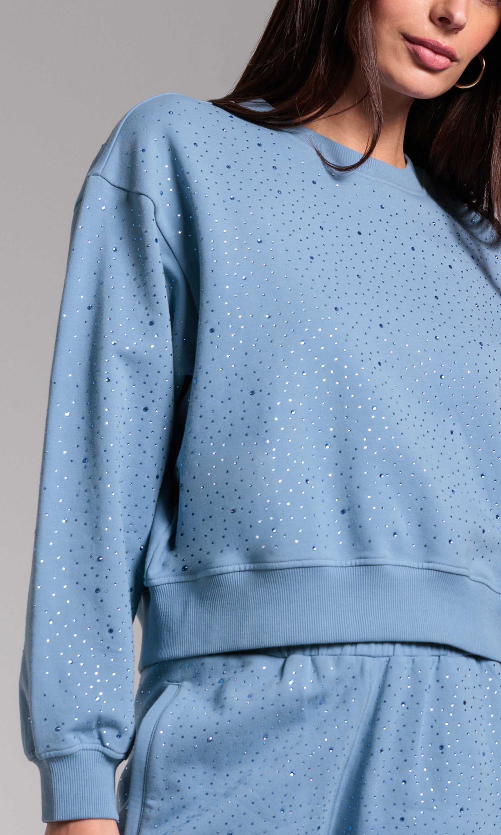 Blue sweatsuit with rhinestones worn by a person against a neutral background