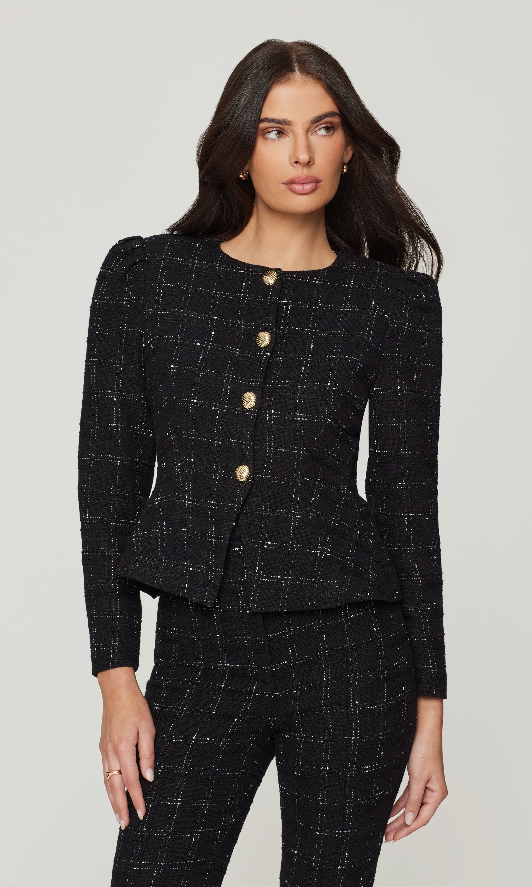 Woman wearing a black checkered suit with gold buttons on a white background
