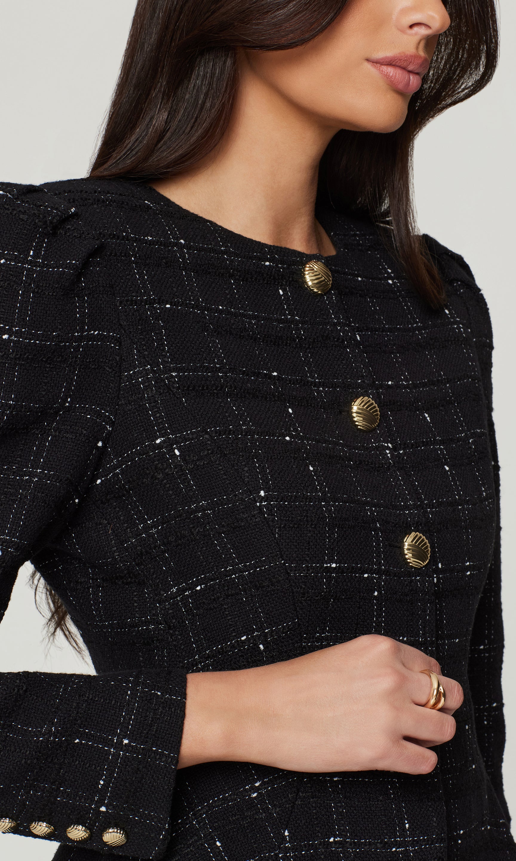 Close-up of black checkered jacket with gold buttons worn by a person on a white background