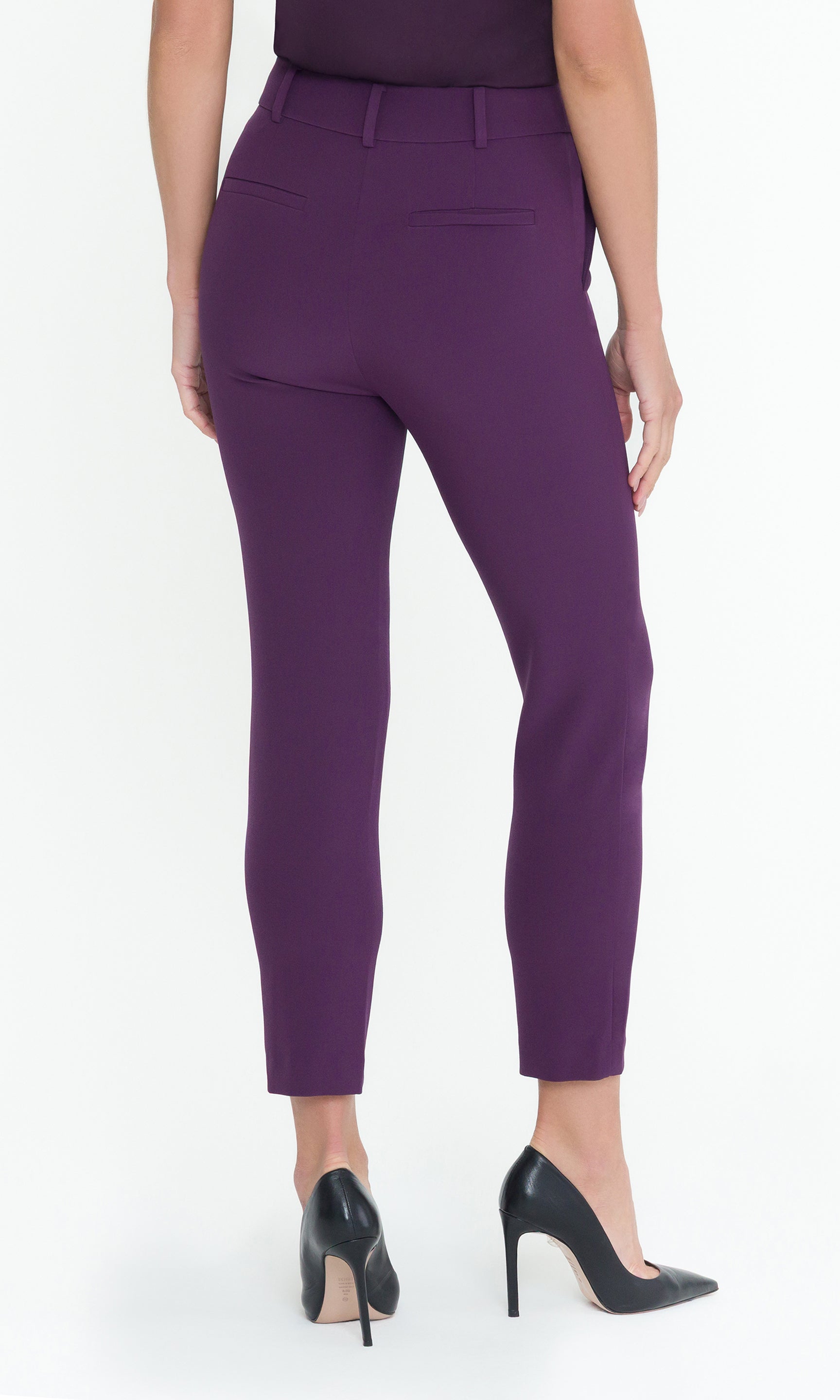 Back view of model wearing purple pants with a matching top and black heels on a white background