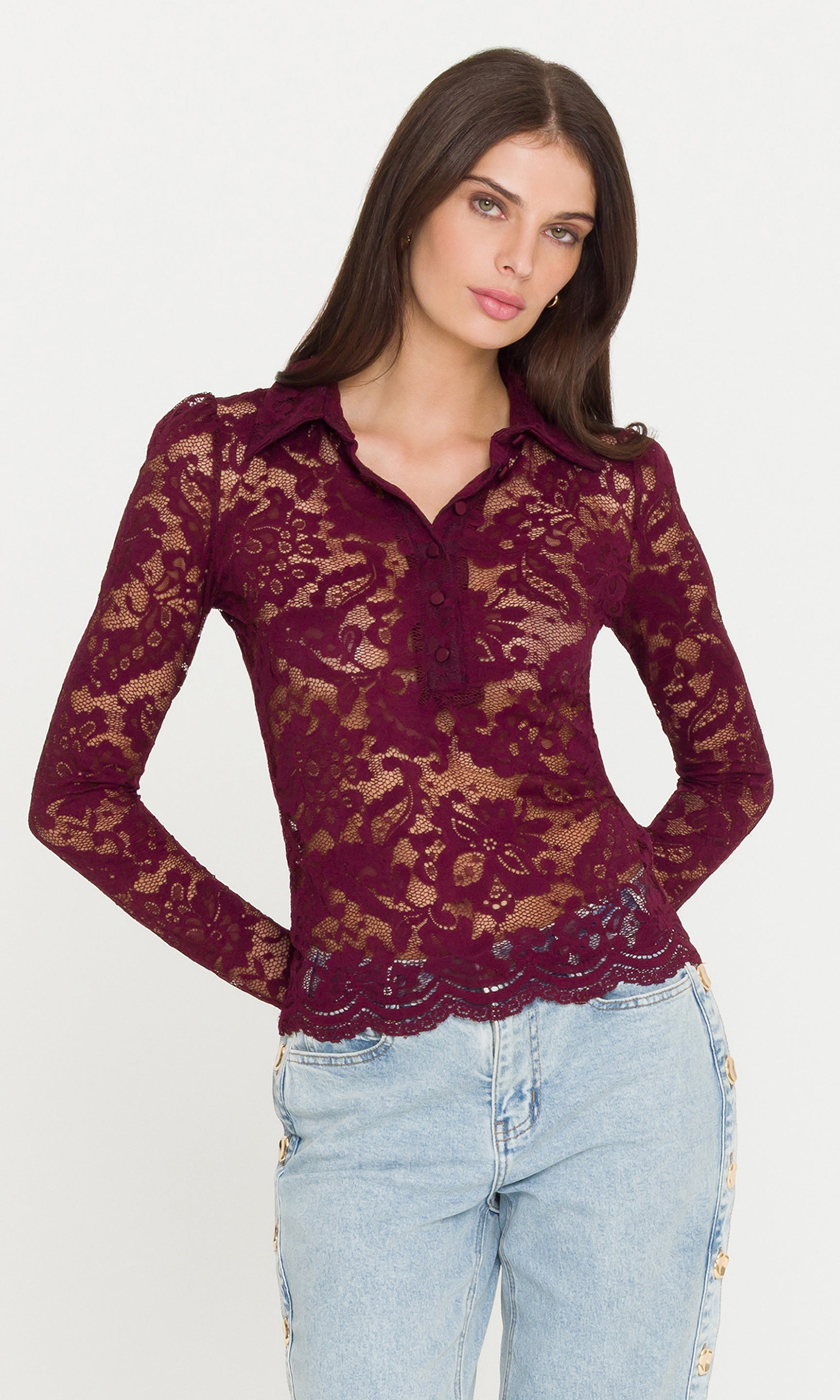 Woman wearing a burgundy lace blouse and light blue jeans on a white background