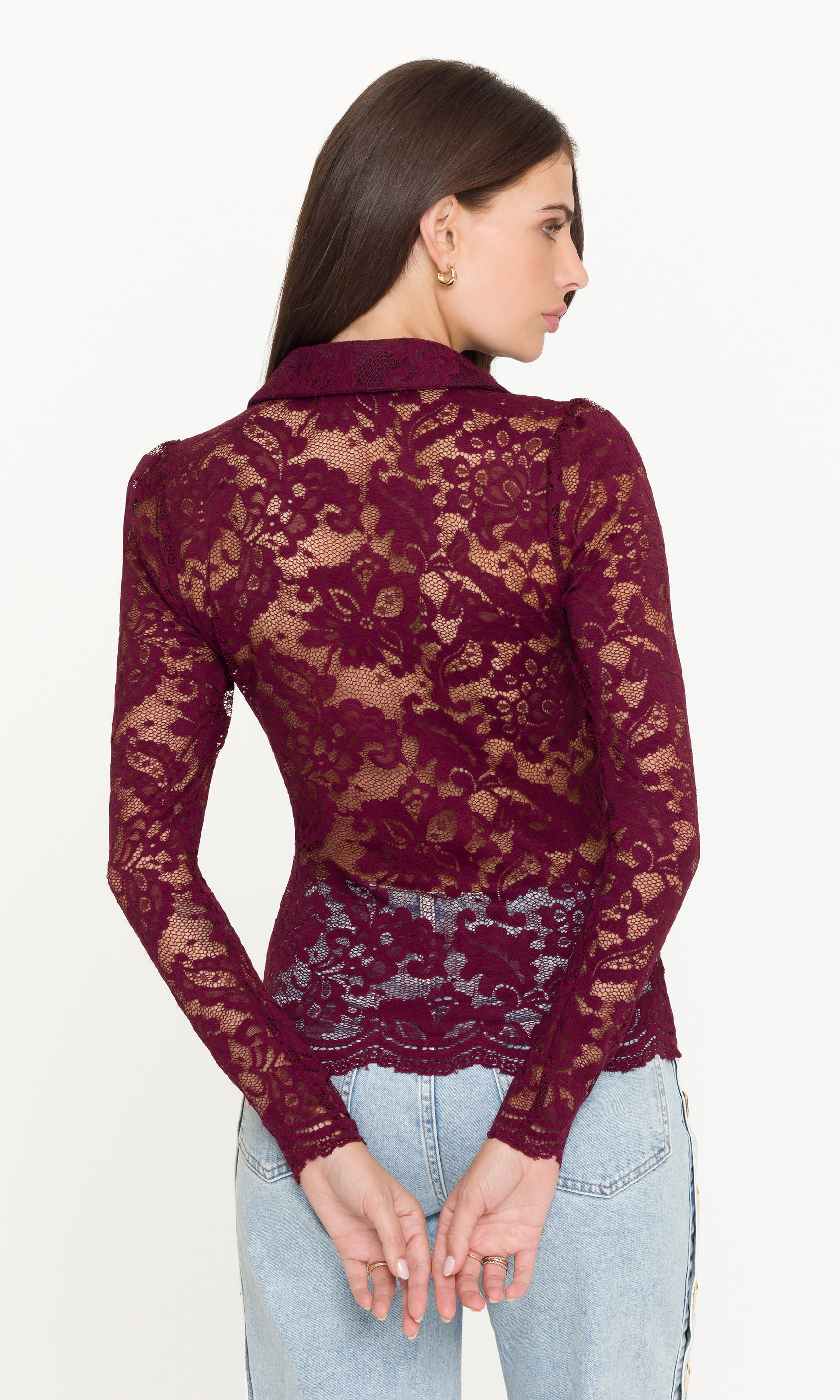 Back view of woman wearing a burgundy lace top with light blue jeans on a white background