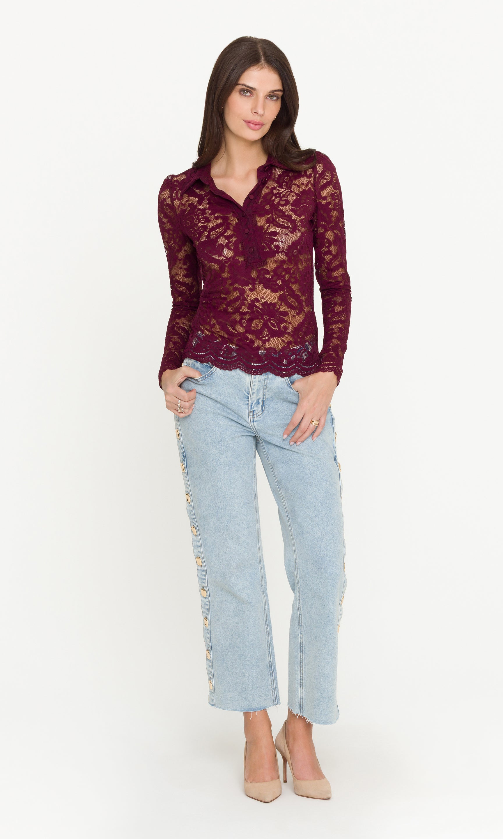 Full body image of woman wearing a burgundy lace top and light blue jeans on a white background