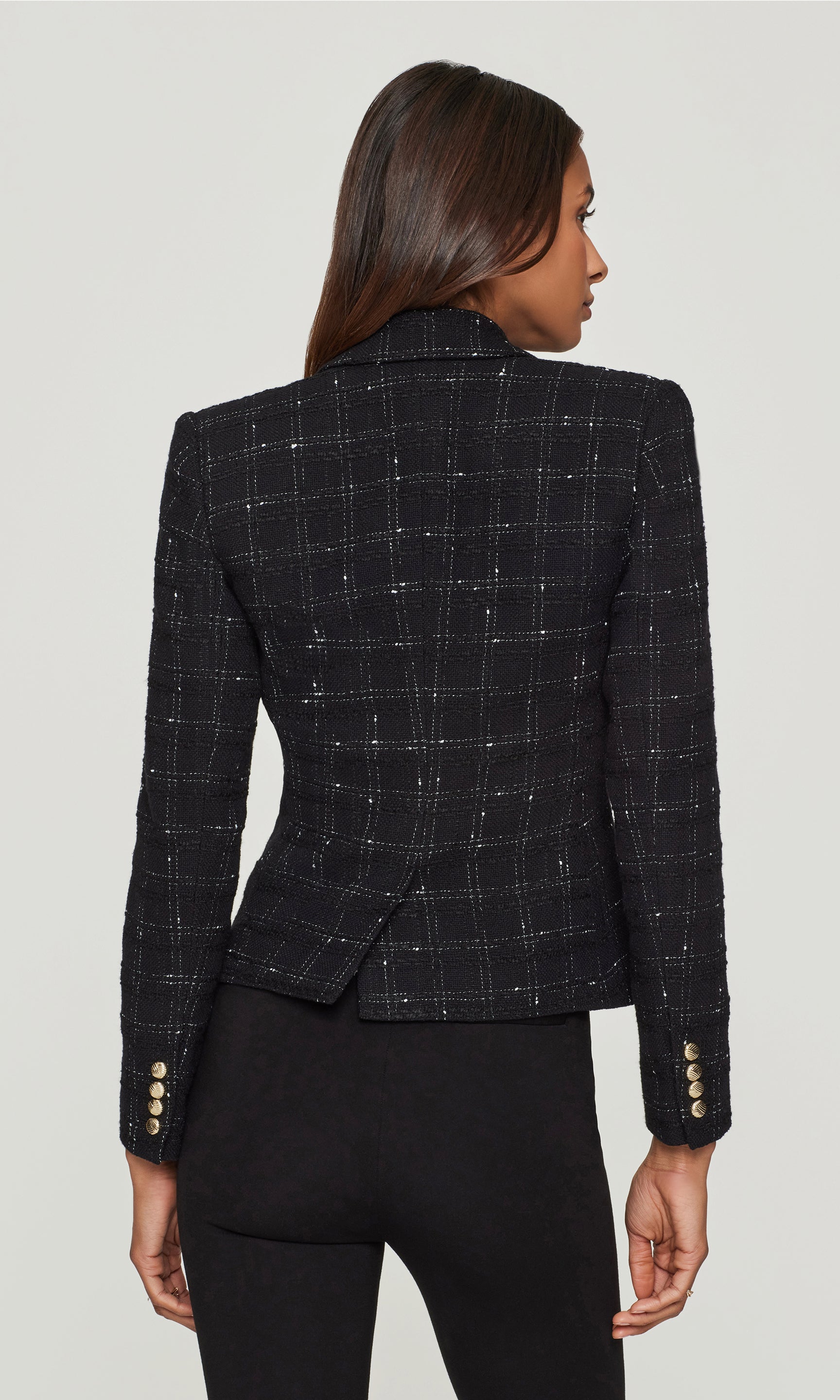 Back view of black checkered blazer worn by a model on a plain background