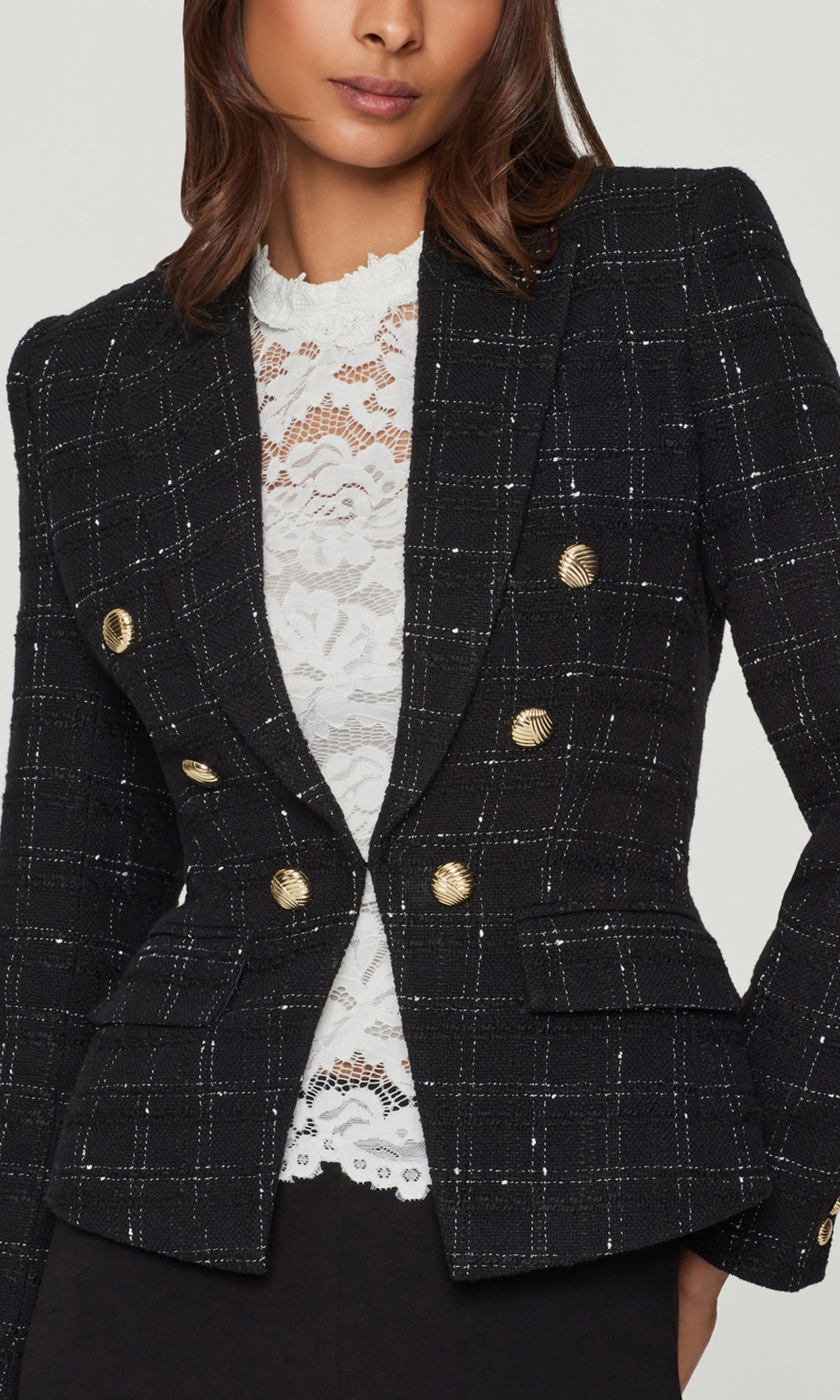 Close-up of black checkered blazer with gold buttons worn by a person on a light gray background