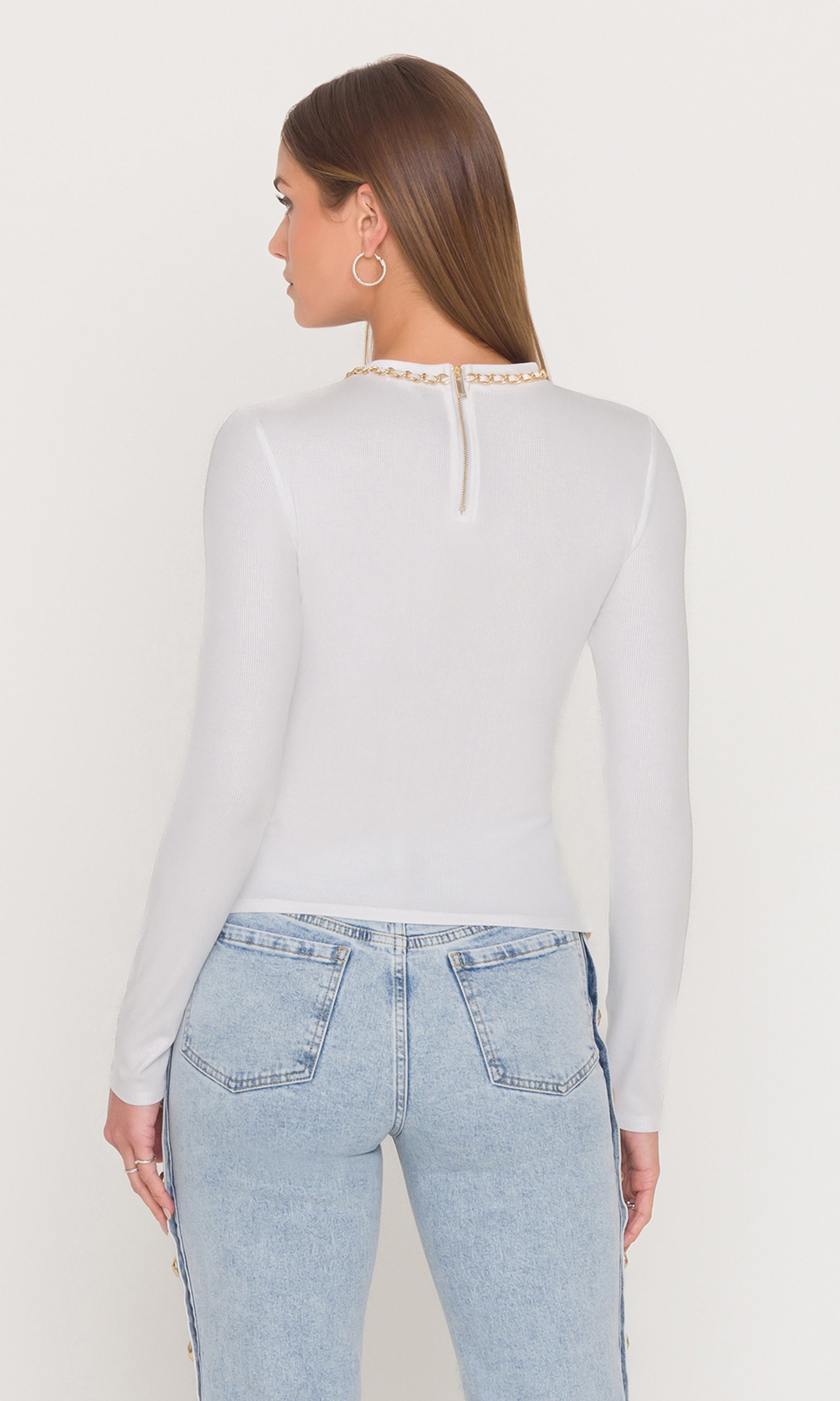 Back view of woman wearing a white long-sleeve top and light blue jeans on a plain background