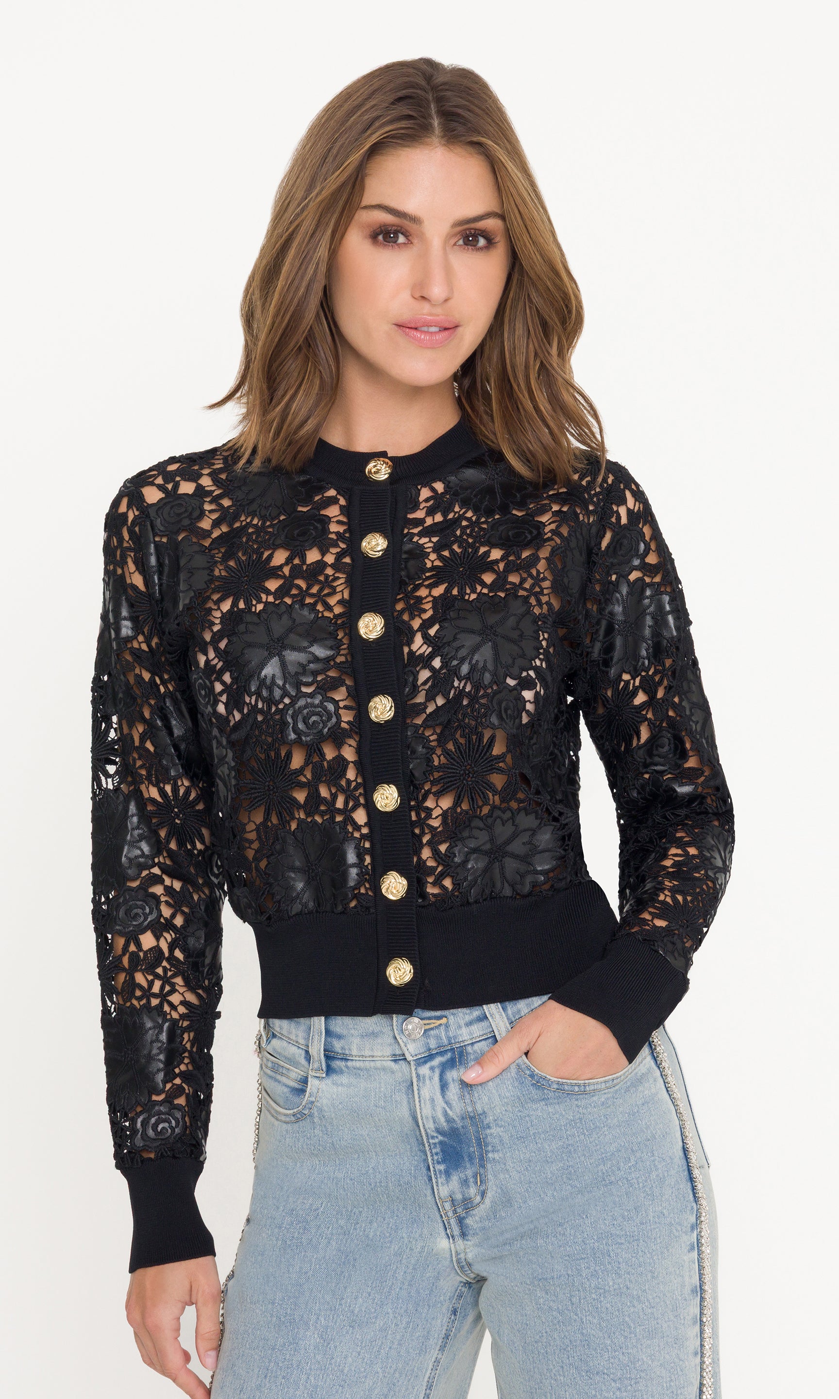Woman wearing a black vegan leather and lace cardigan with gold buttons on a white background