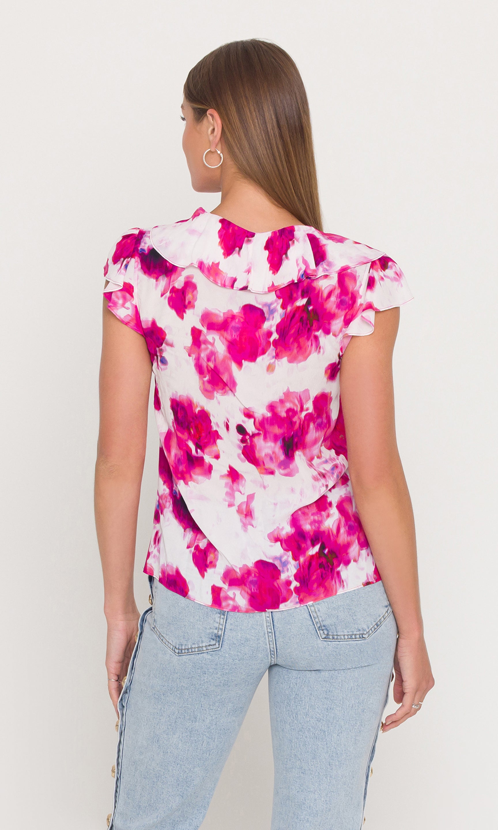 Back view of woman wearing a pink floral top and light blue jeans on a white background