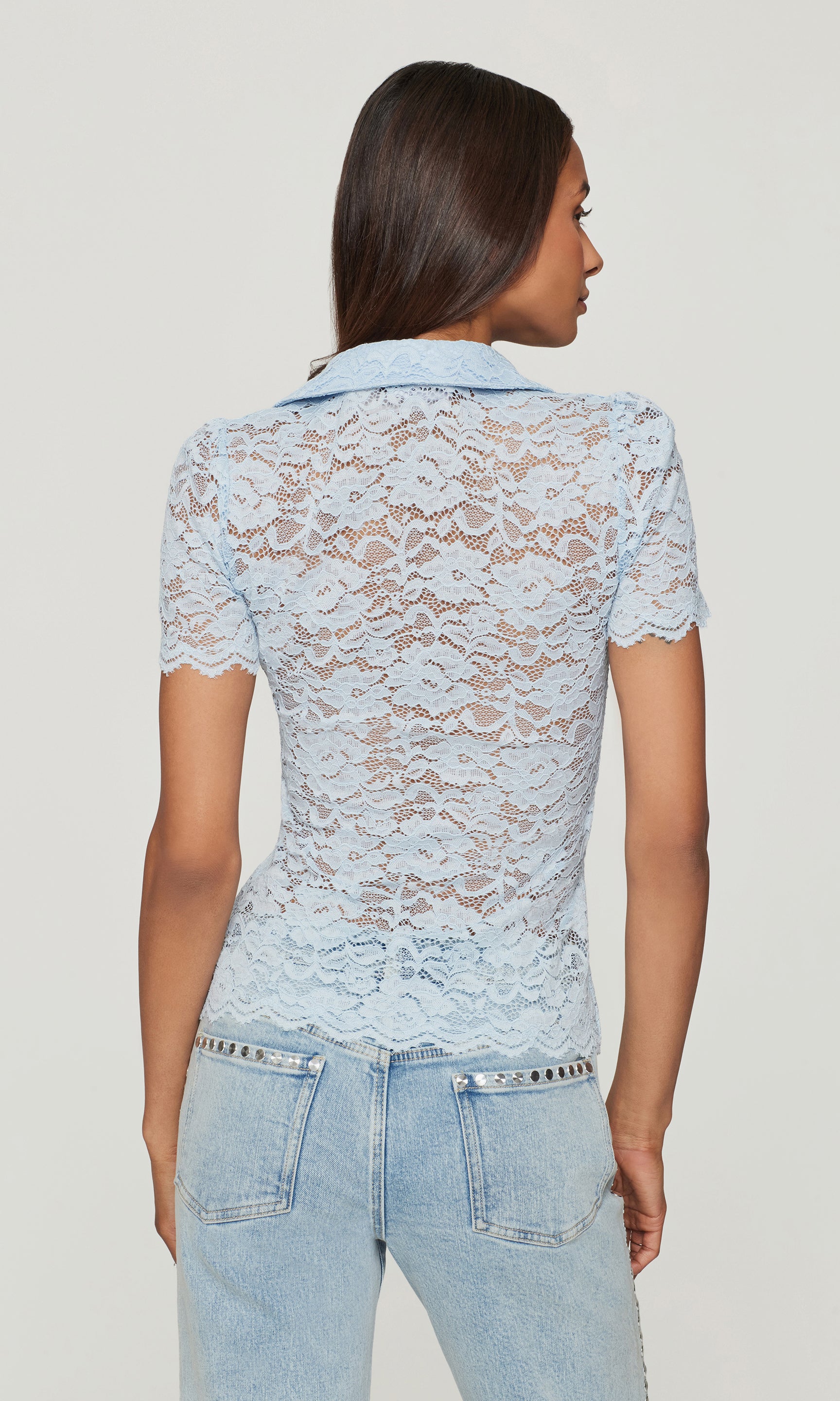 Woman wearing a light blue lace top and jeans on a plain background