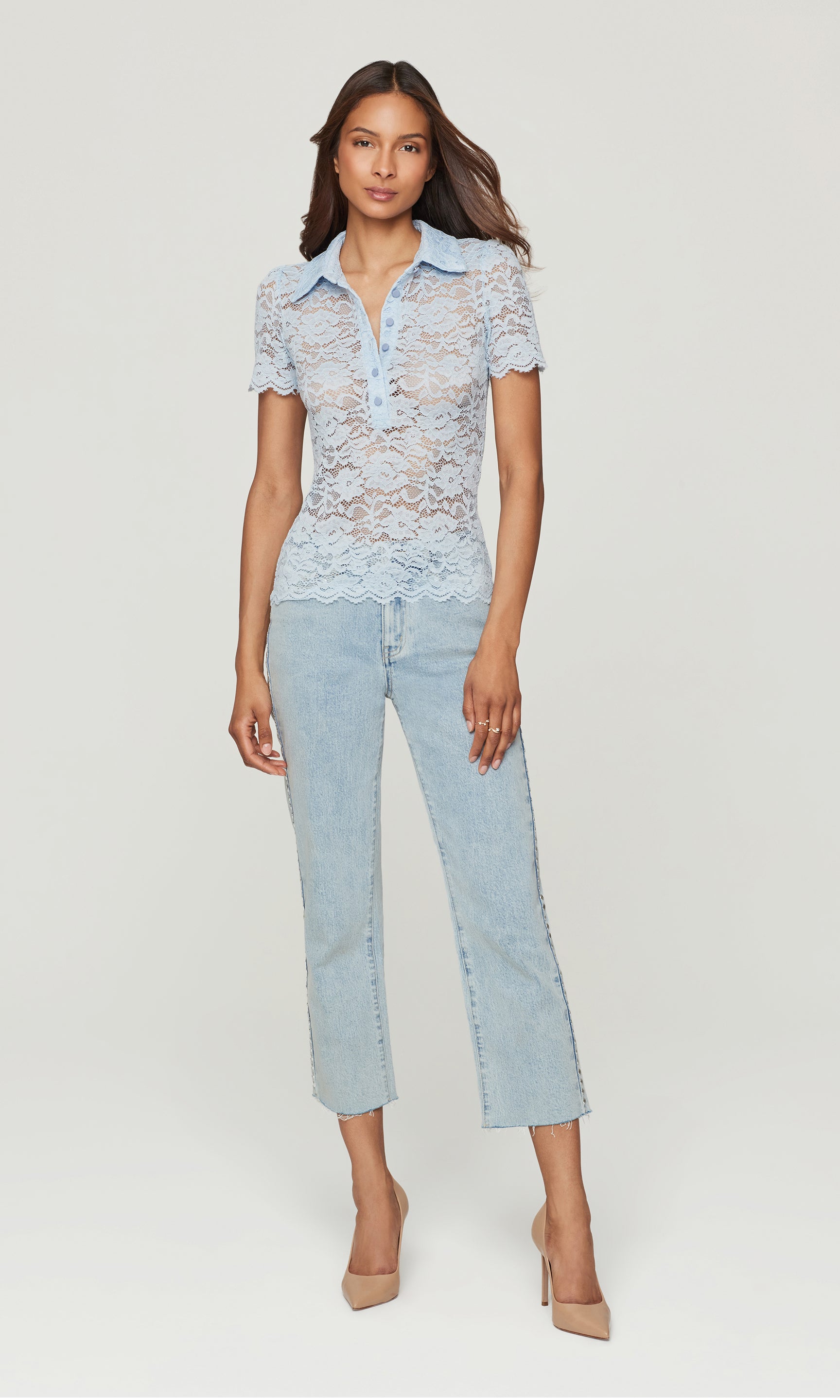 Woman wearing a light blue lace top and jeans on a white background
