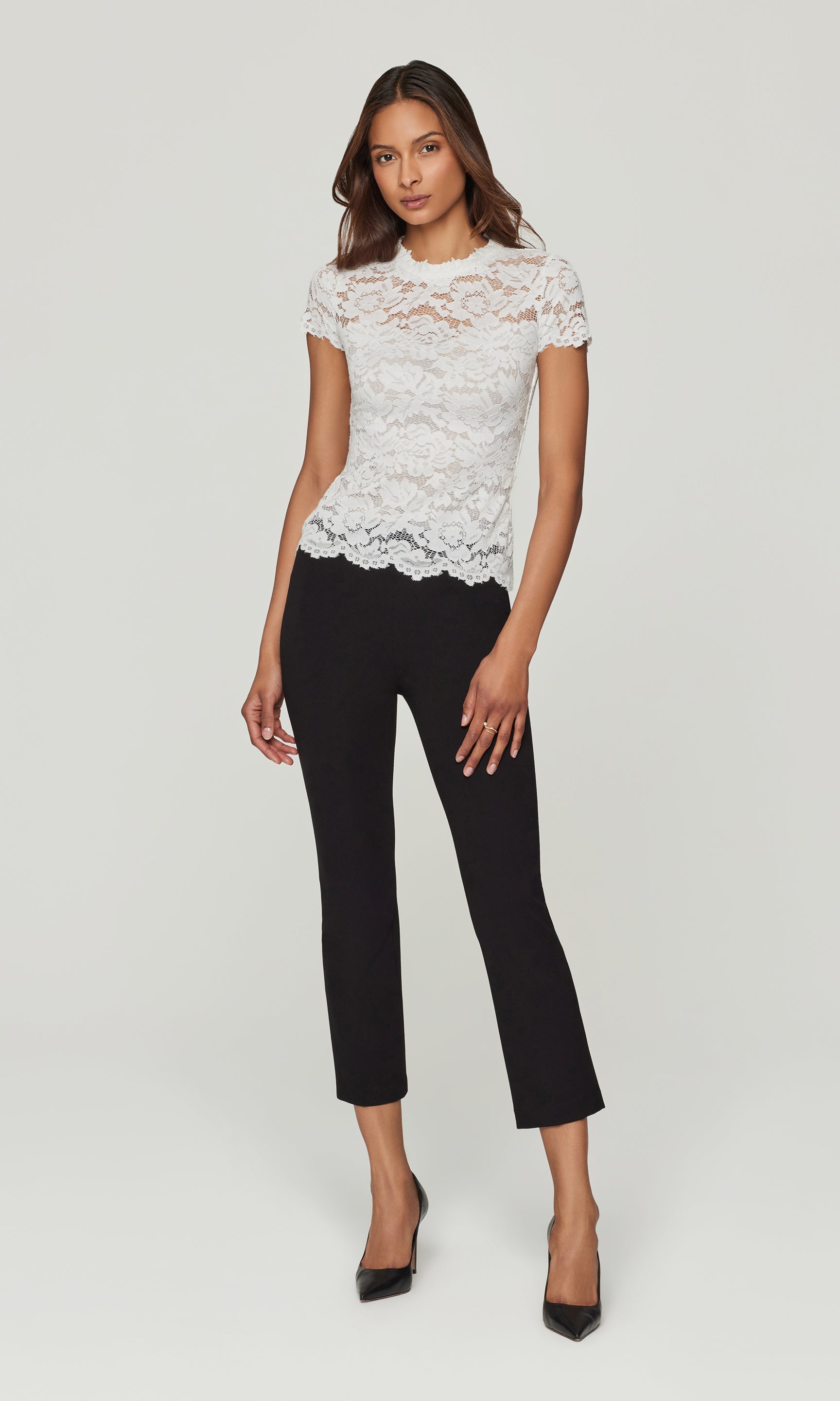 Woman wearing a white lace top and black pants on a light gray background