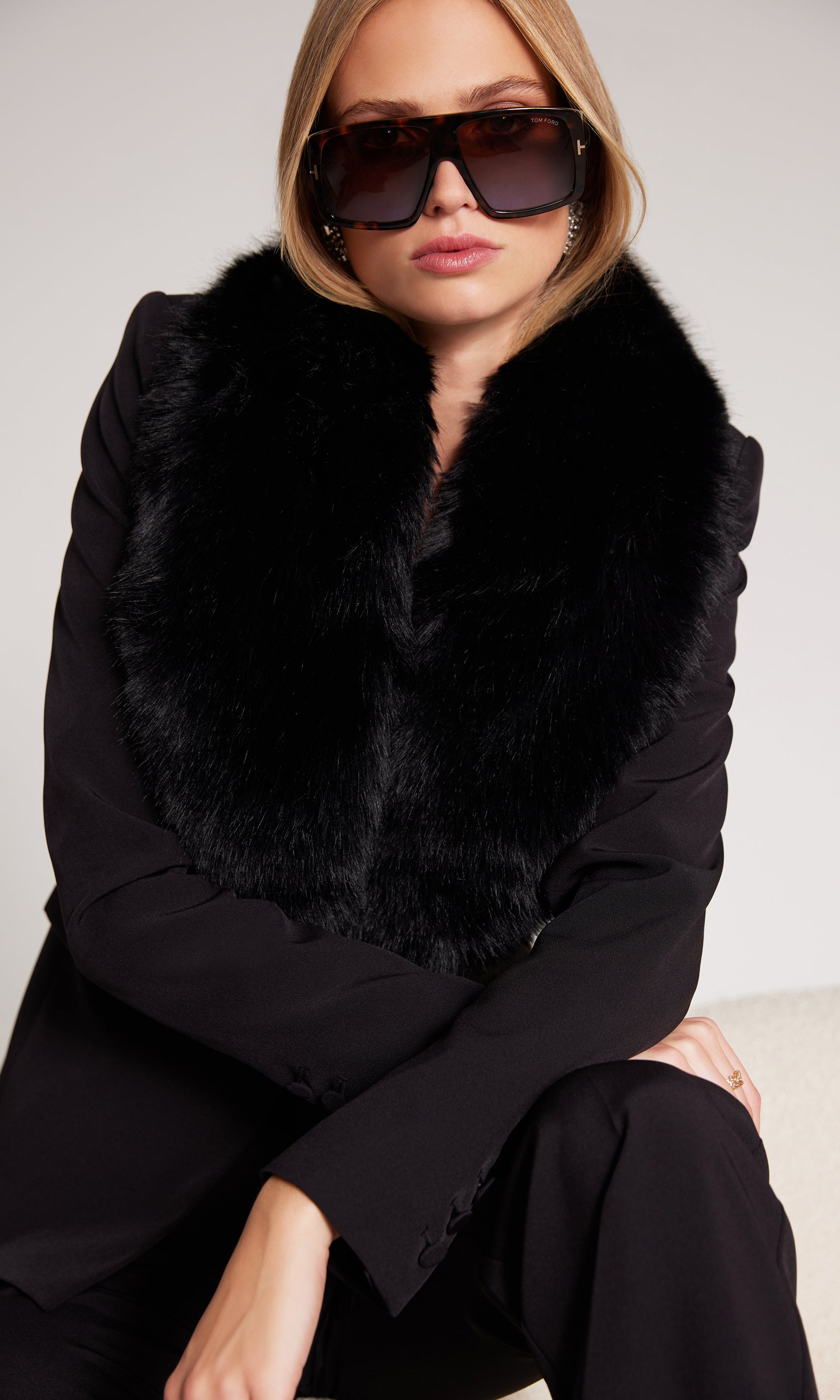 Woman wearing a black fur collar and sunglasses against a plain background