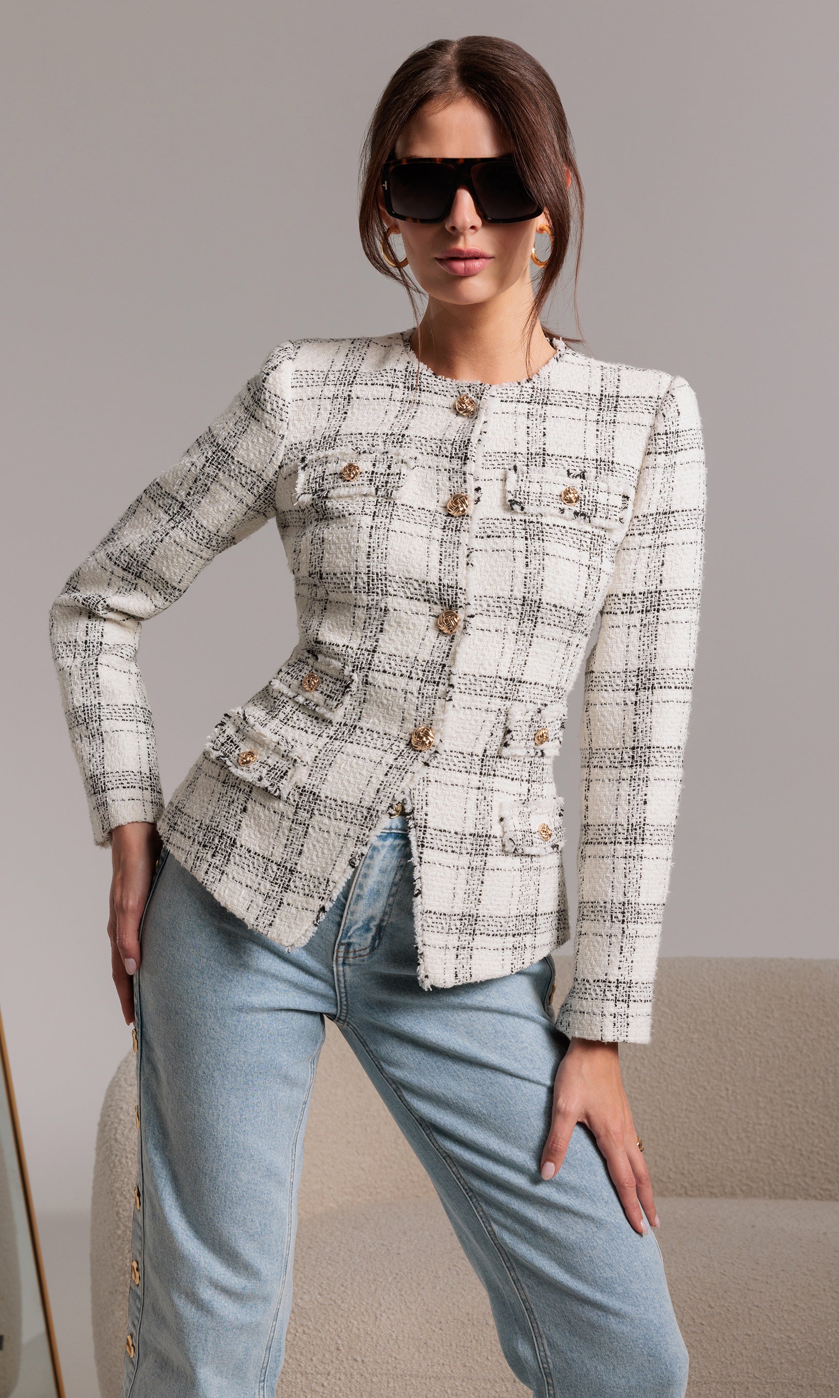 Woman wearing a patterned jacket and light blue jeans against a neutral background
