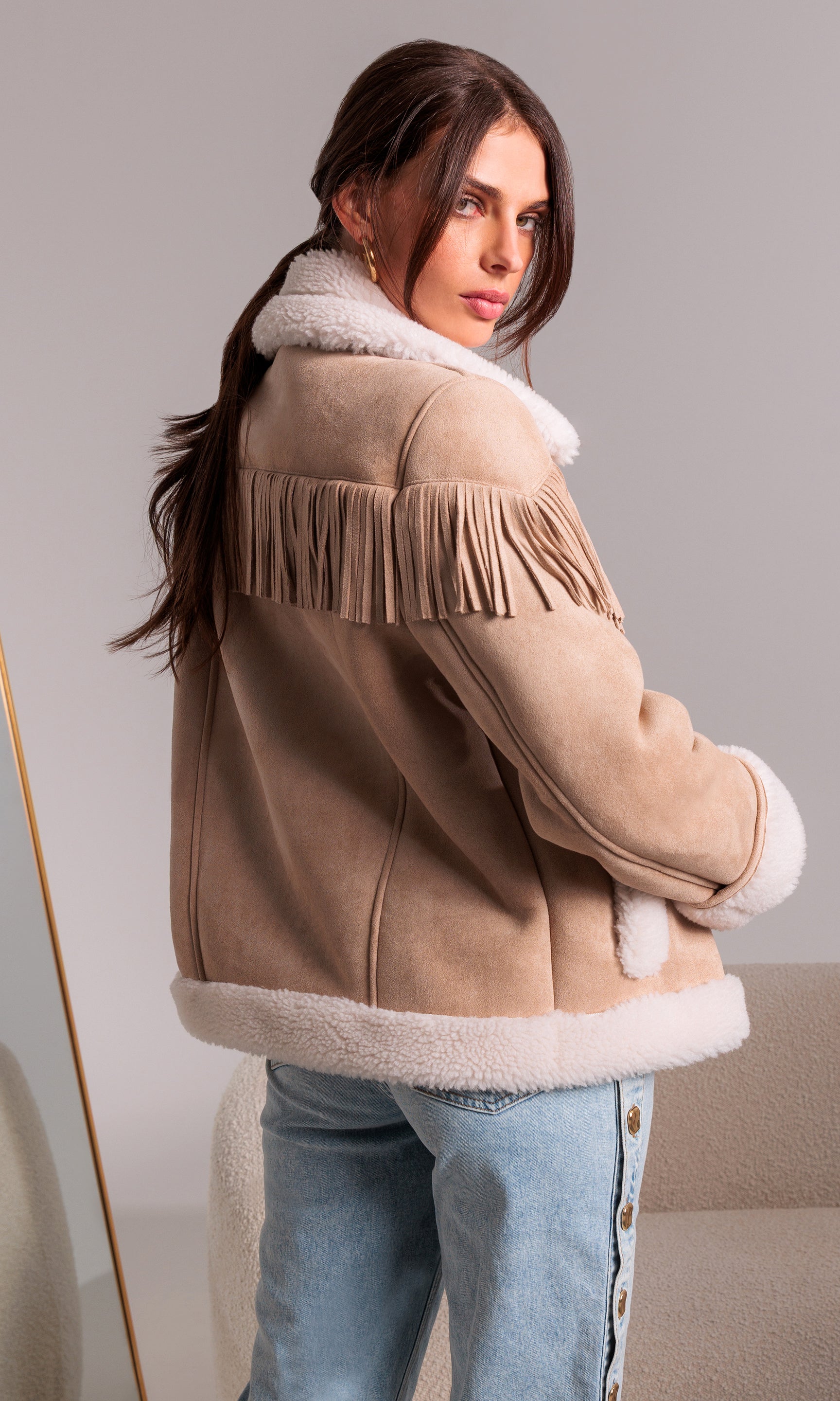 Woman wearing a beige shearling jacket with white fur trim on a neutral background