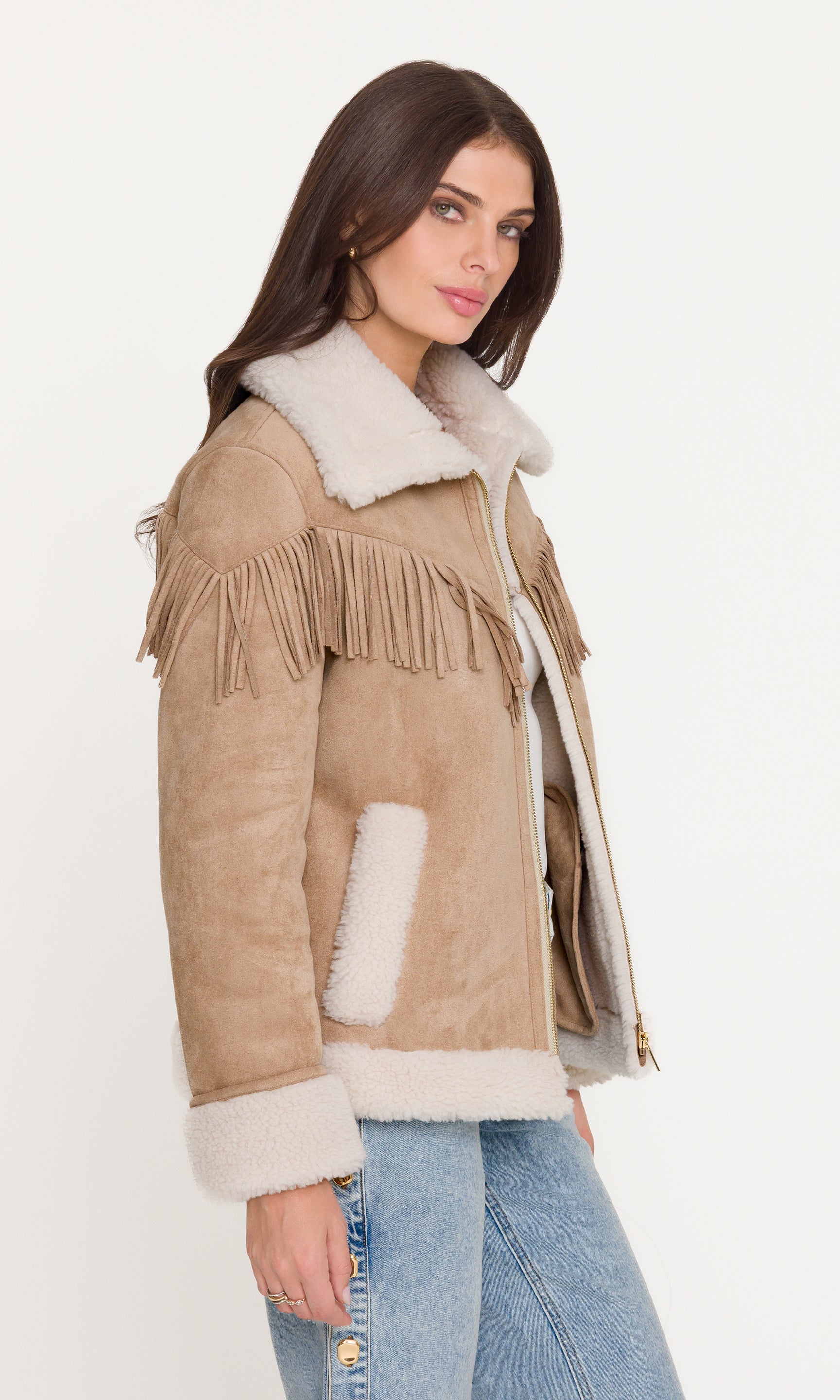 Side view of woman wearing a beige suede jacket with white fur trim on a white background