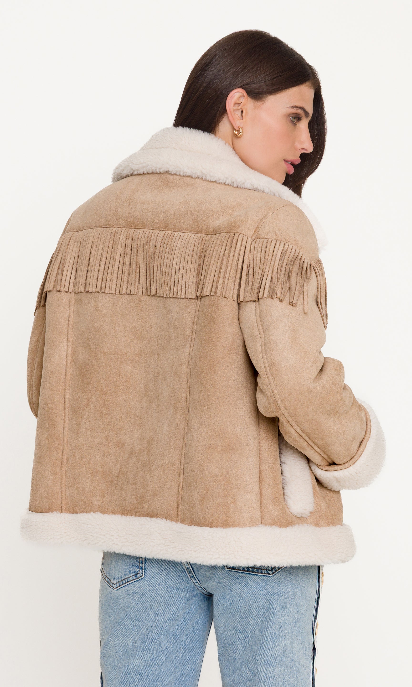 Back view of model wearing a beige shearling jacket with fringes on a white background