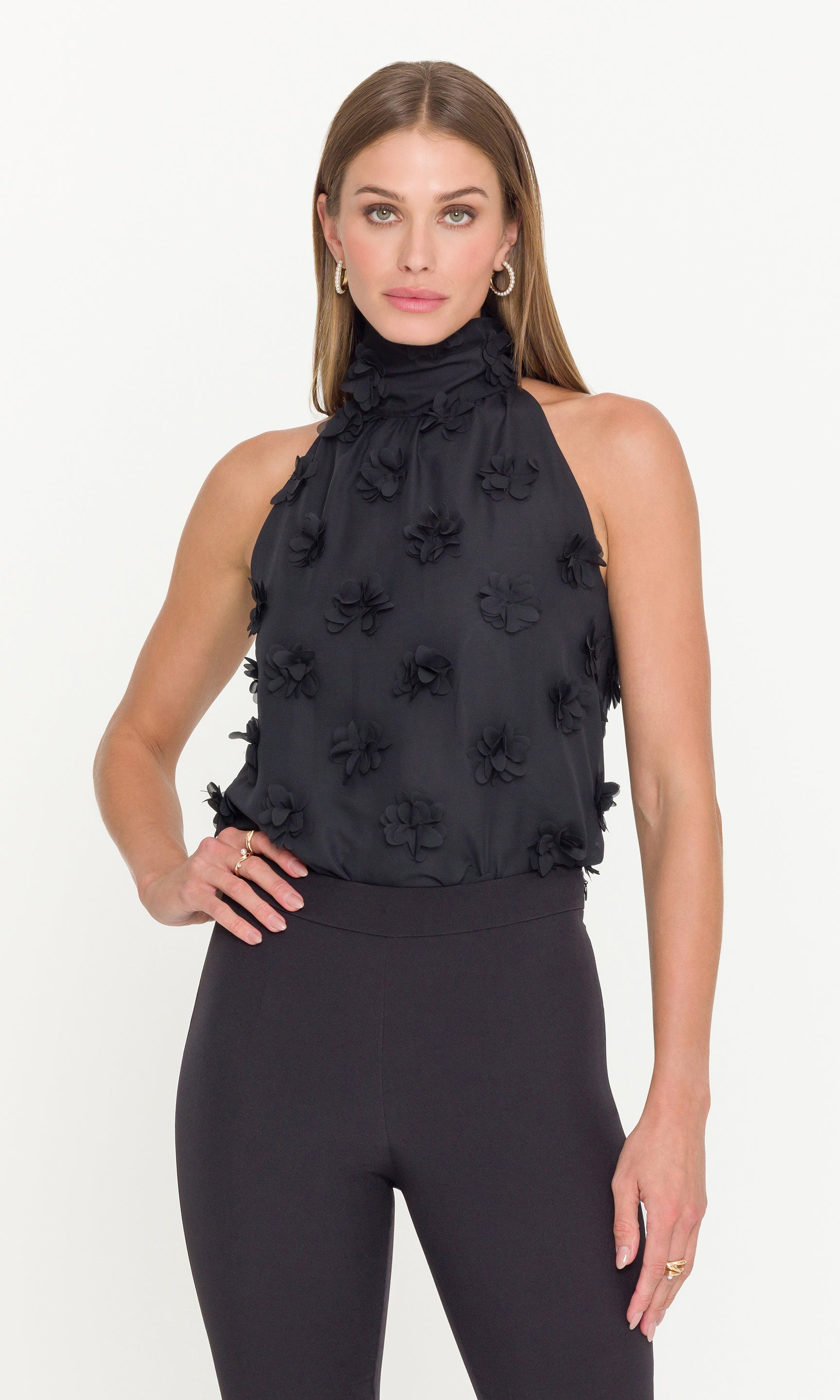 Woman wearing a black halter top with floral embellishments on a white background