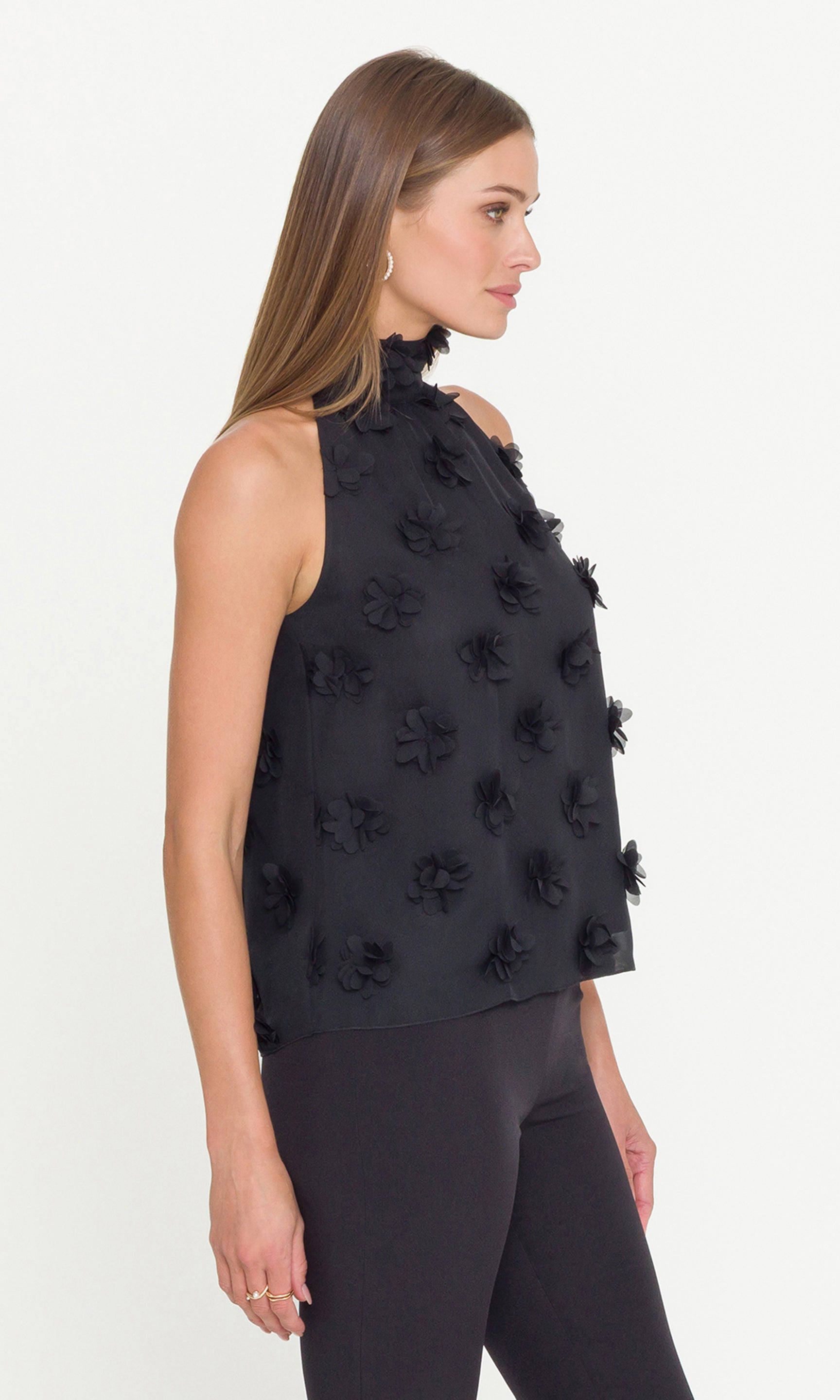 Woman wearing a black sleeveless top with floral embellishments on a white background
