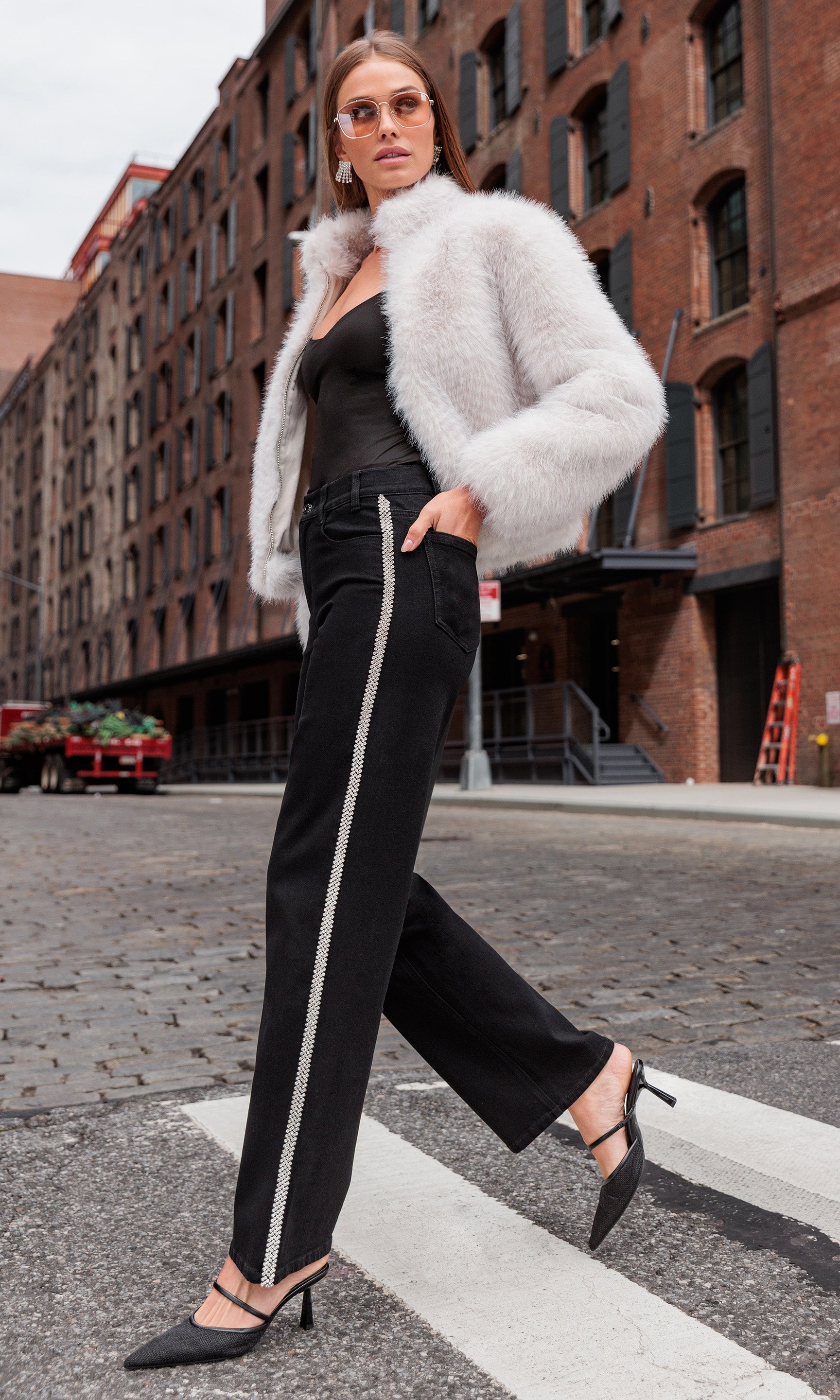 Model wearing a white fur coat, black top and black jeans with crystal embellishments in an urban setting