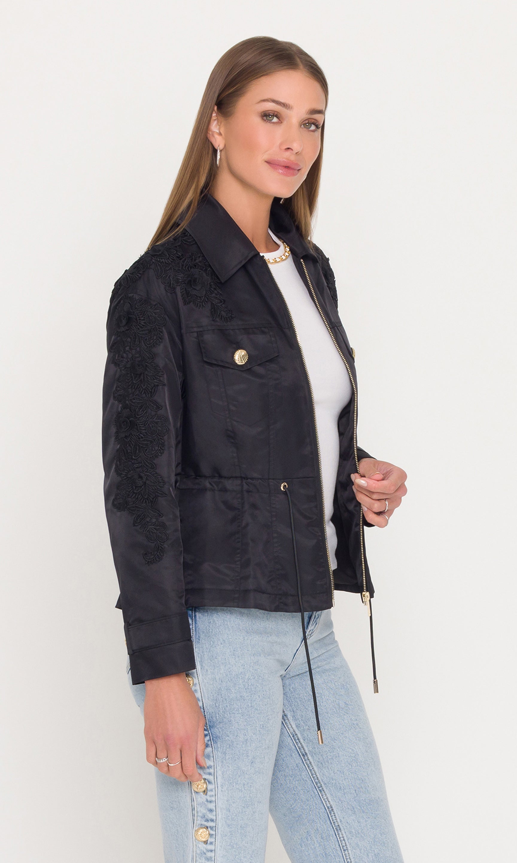 Side view of woman wearing a black jacket with floral embroidery and gold buttons on a white background