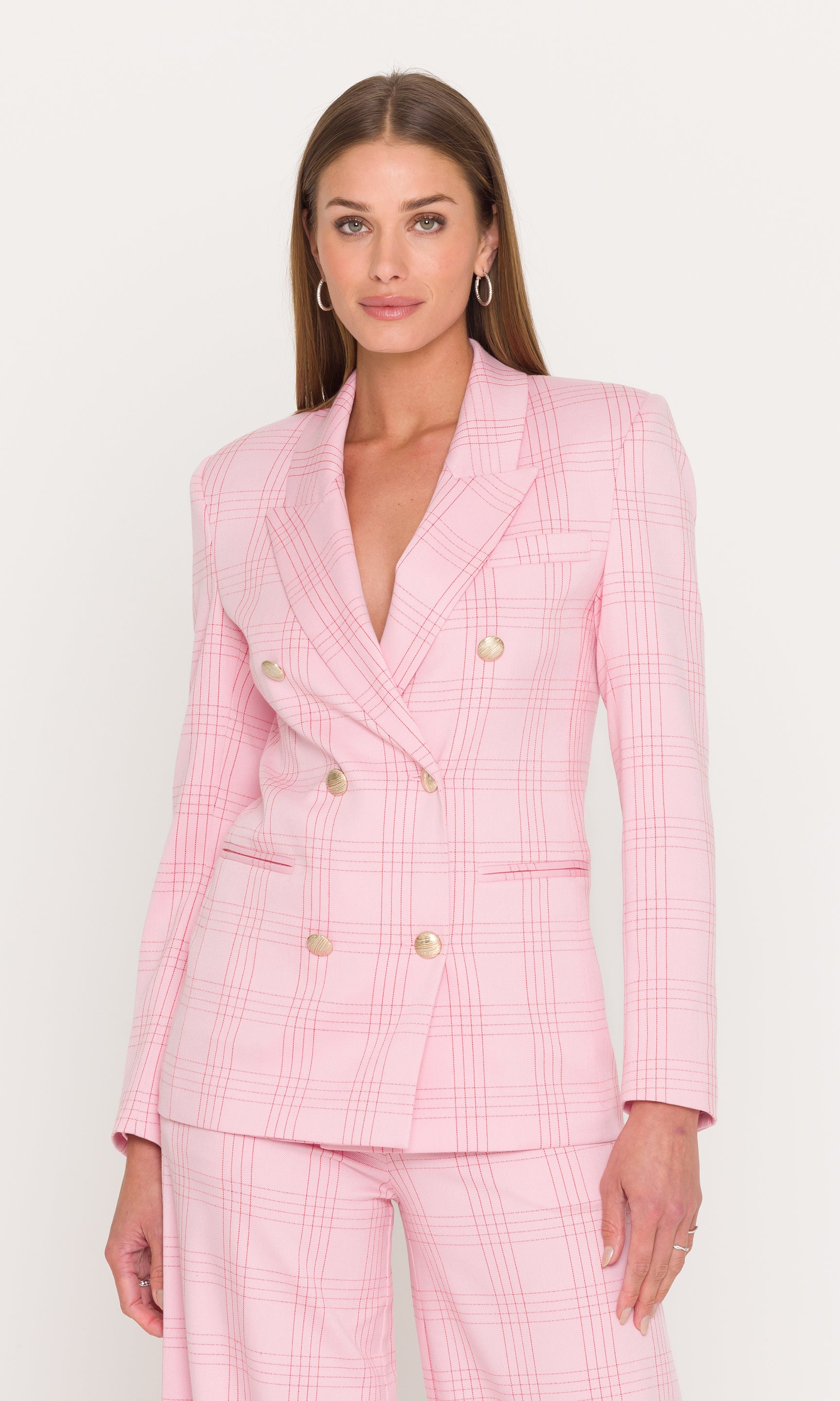 Woman wearing a pink checkered blazer matching trousers against a white background