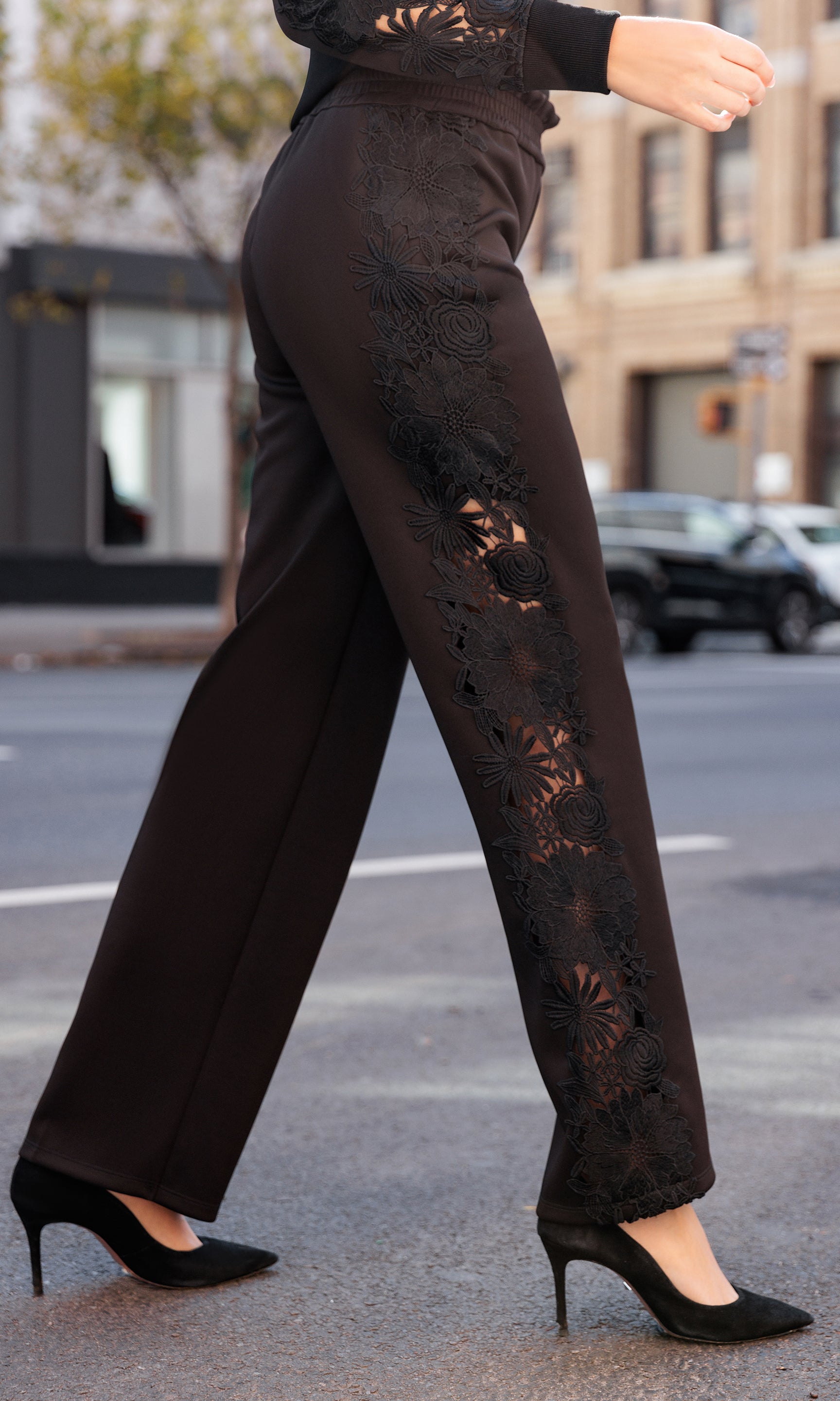 Person wearing black lace pants walking on a street.