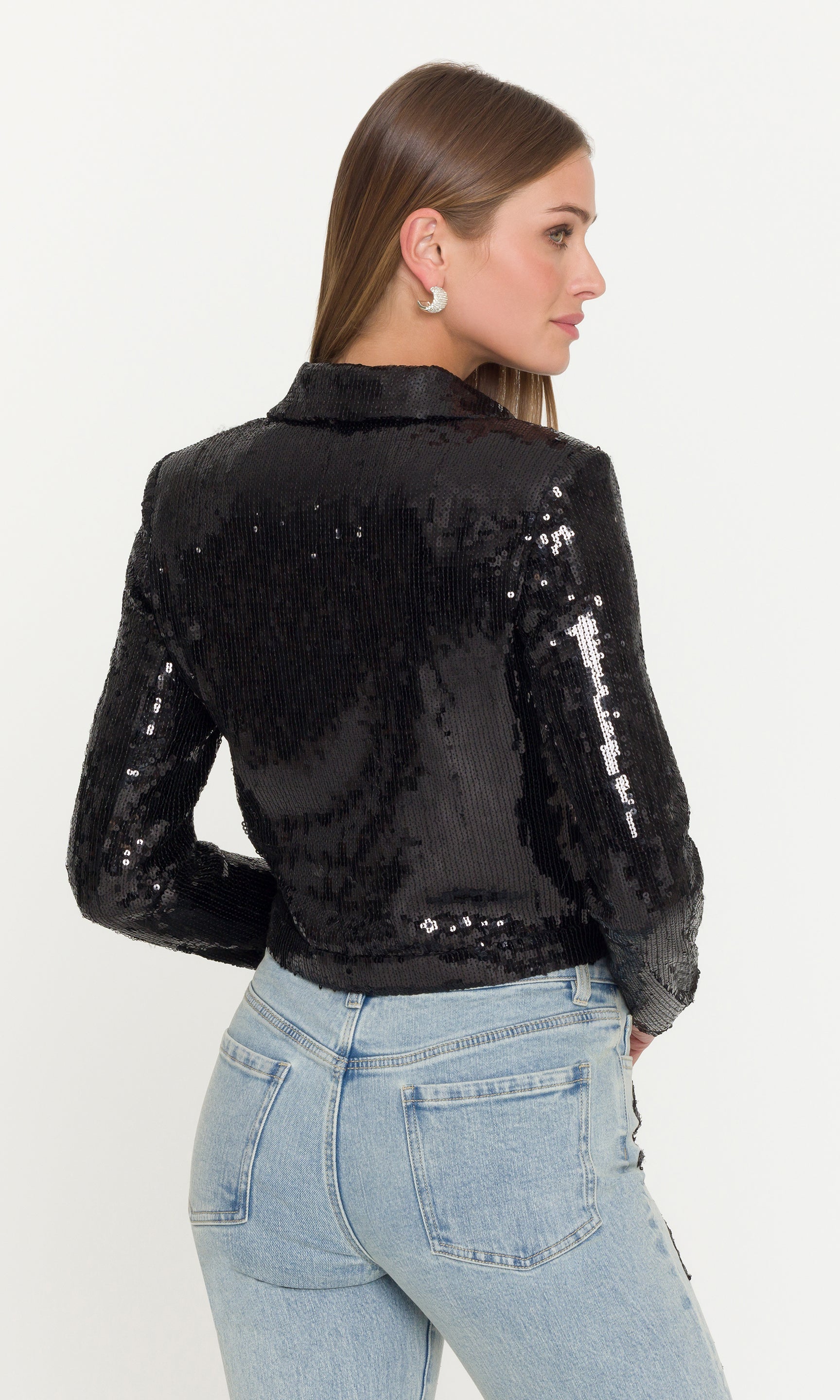 Back view of woman wearing a black sequin jacket and light blue jeans on a white background