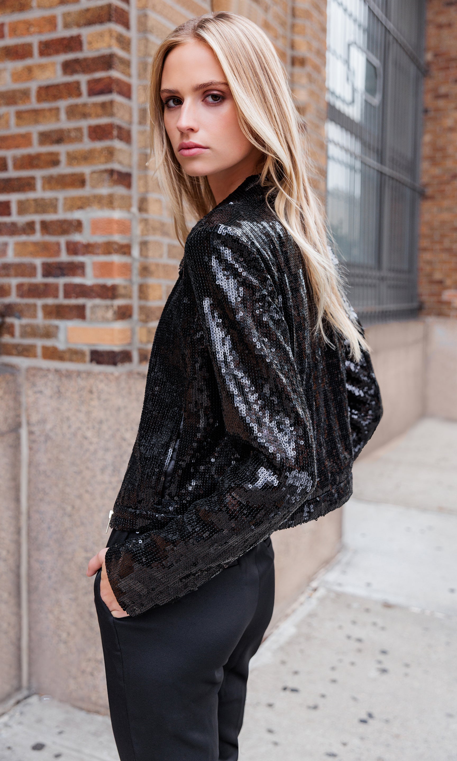 Back view of model wearing a black sequin jacket and black pants outdoors