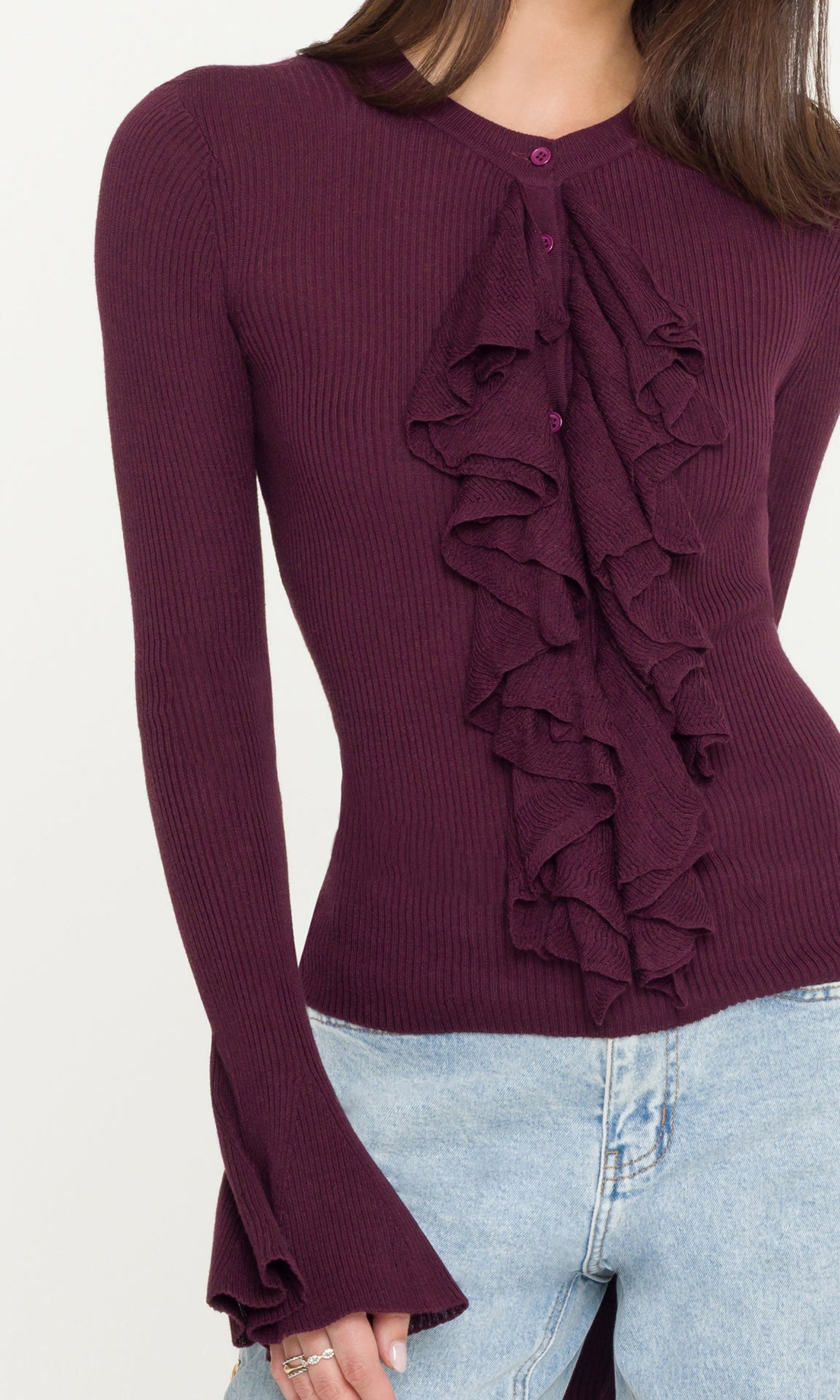 Woman wearing a burgundy ruffled long-sleeve top and light blue jeans on a white background