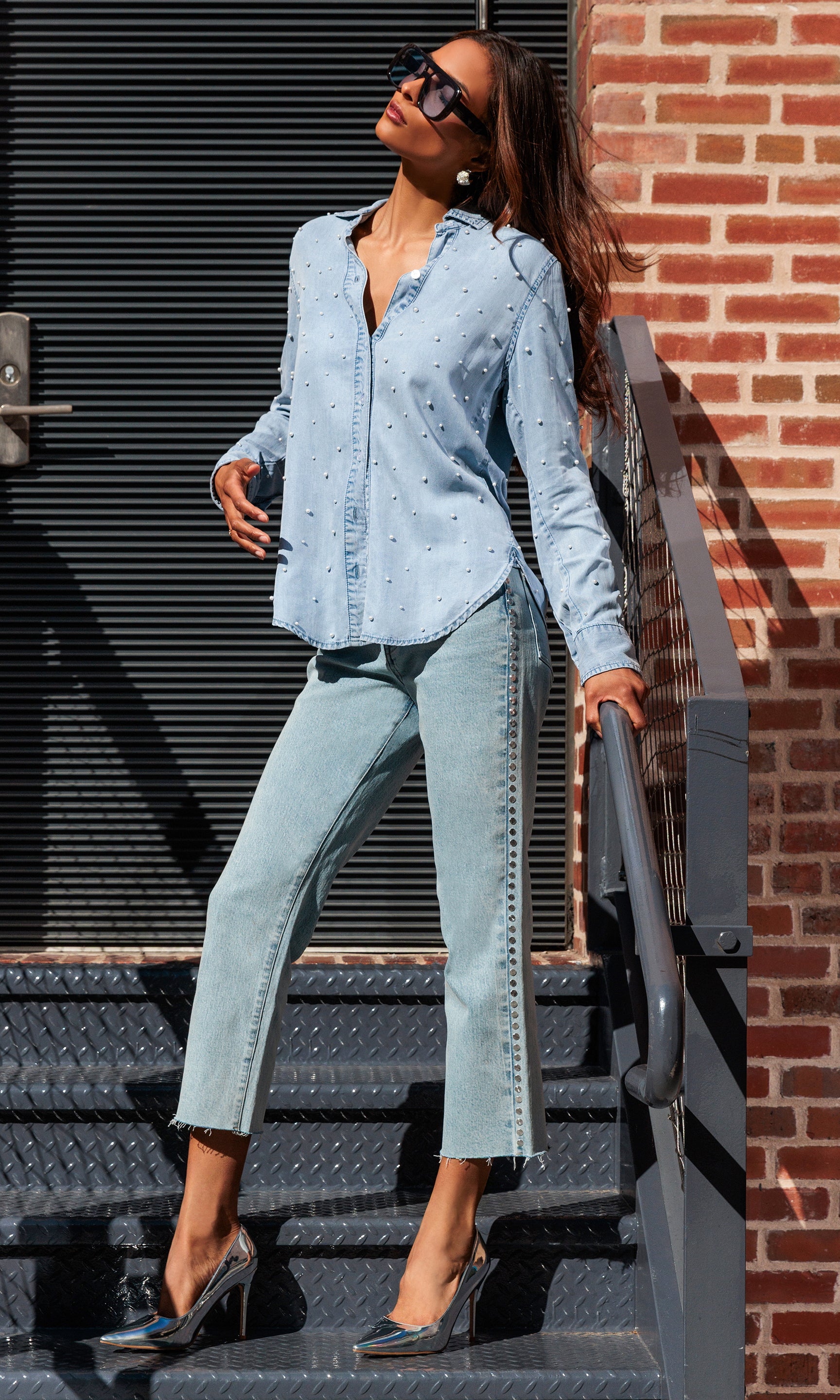 Woman in a light blue outfit standing on a set of stairs against a brick wall.