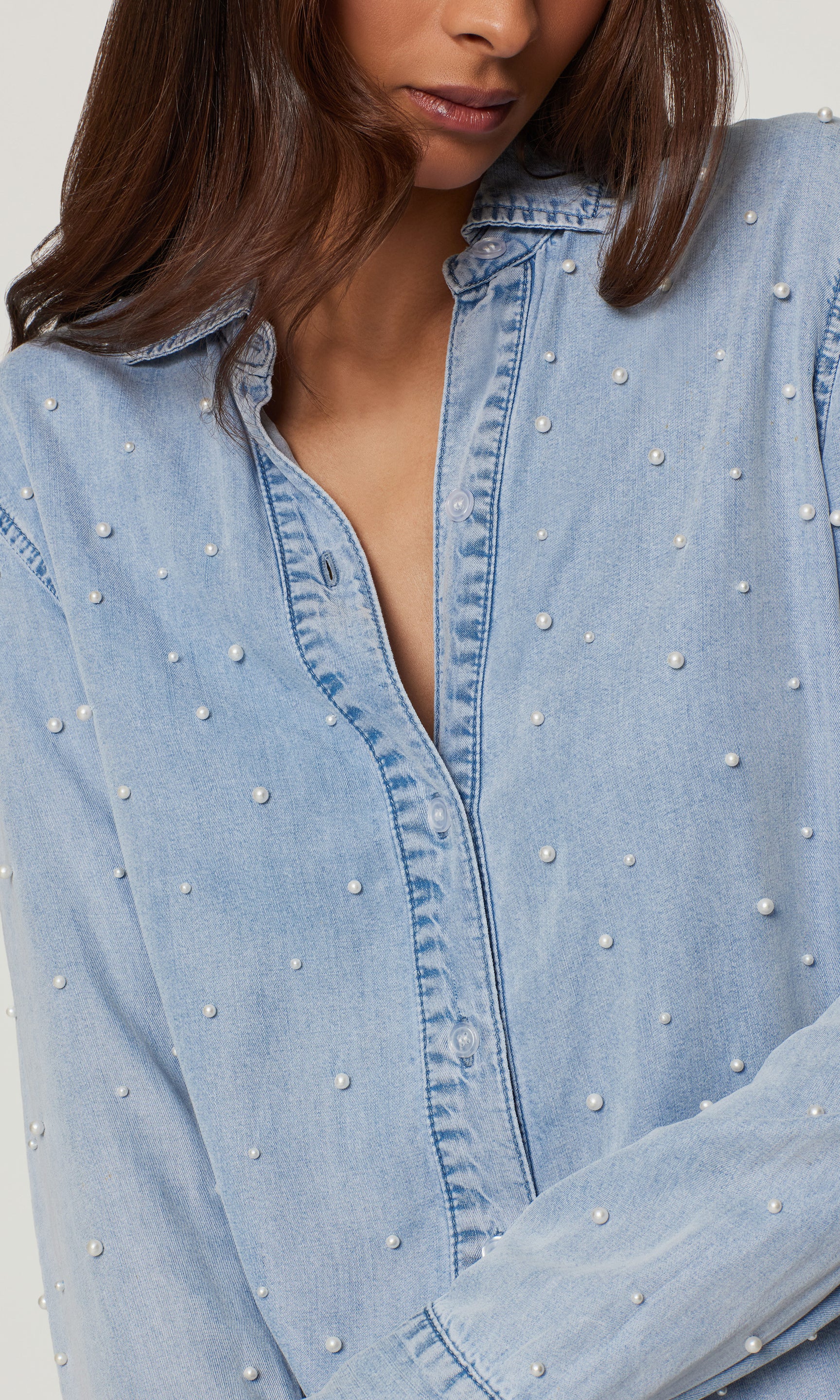 Light blue denim shirt with pearl embellishments on a plain background