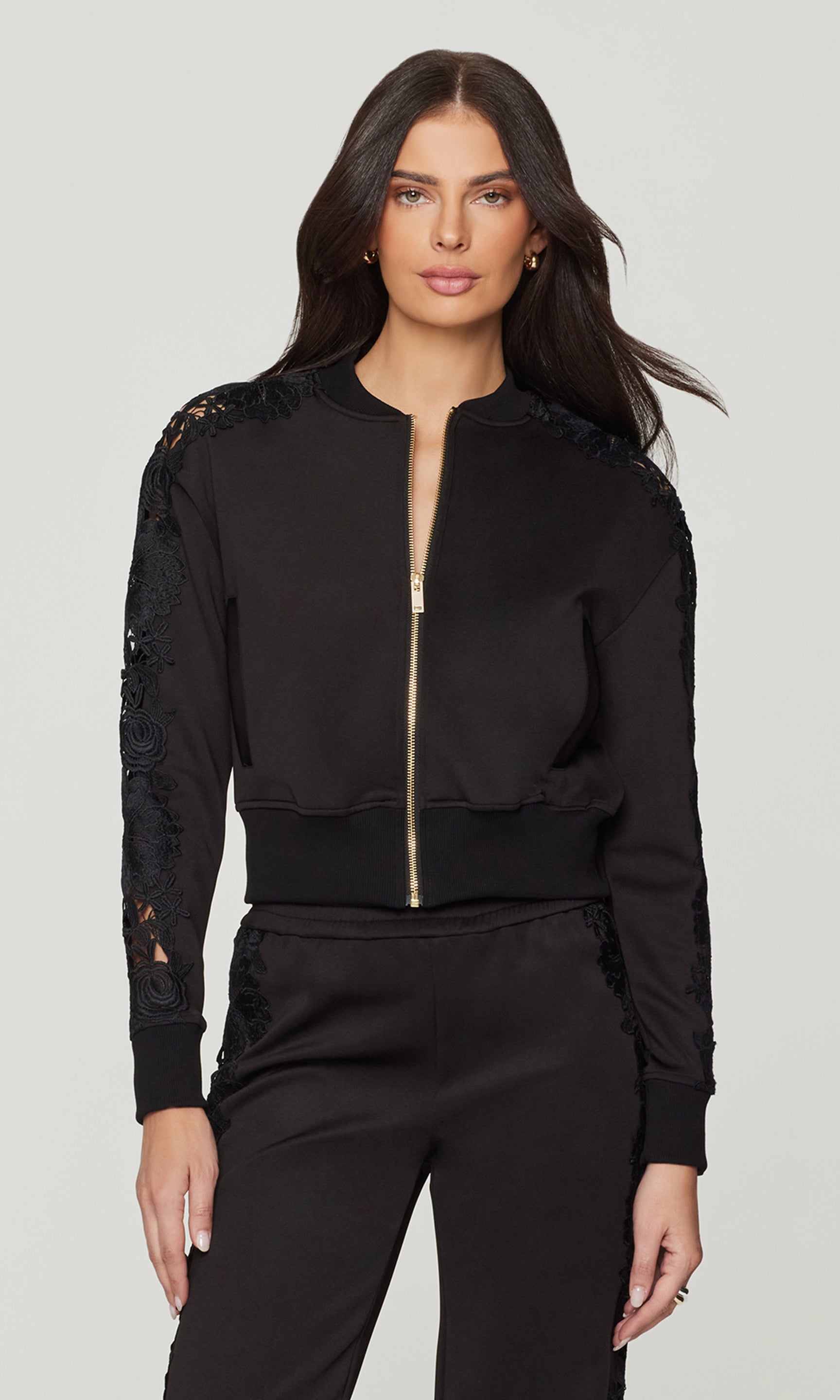 Woman wearing a black bomber jacket with lace sleeves on a white background
