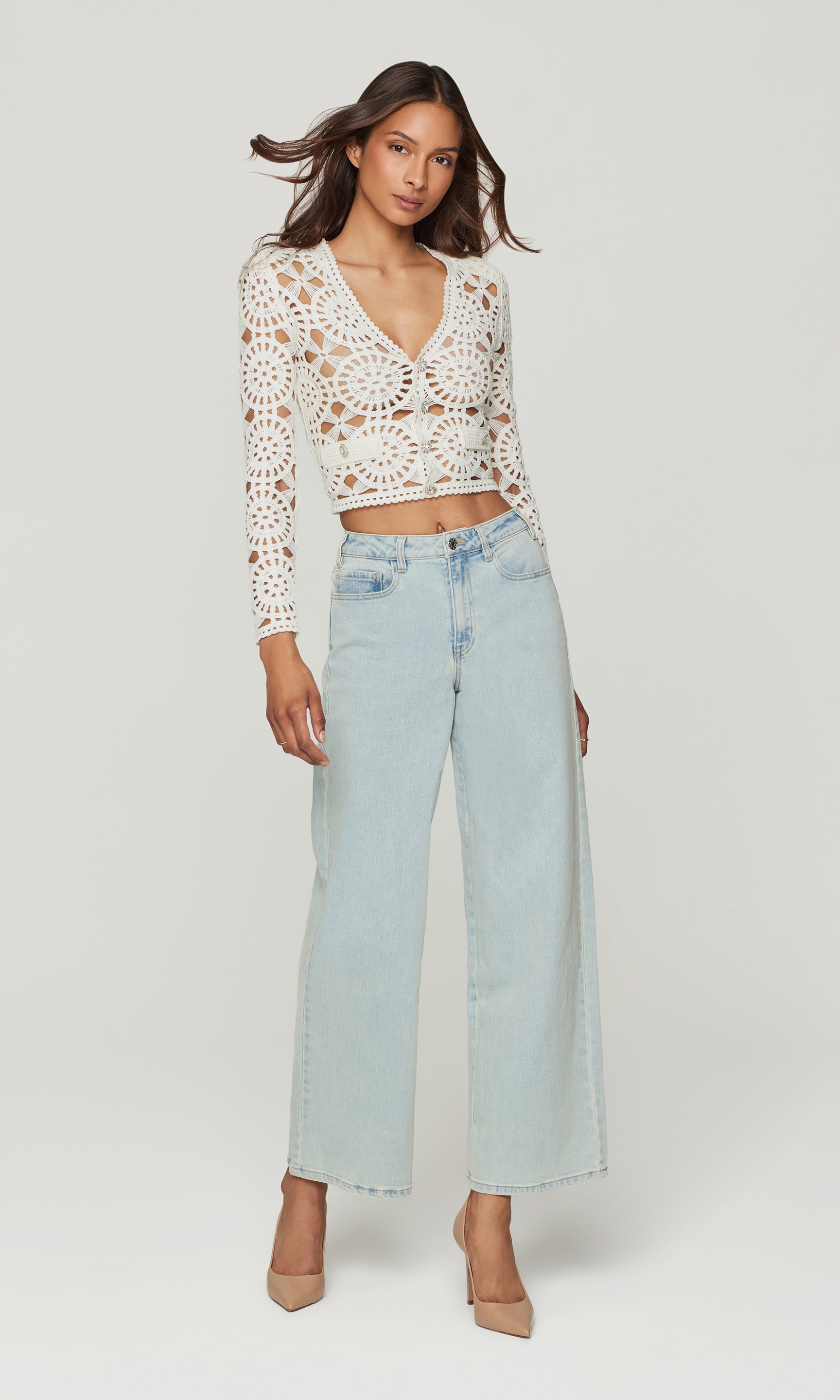 Woman wearing a white crochet top and light blue jeans on a white background