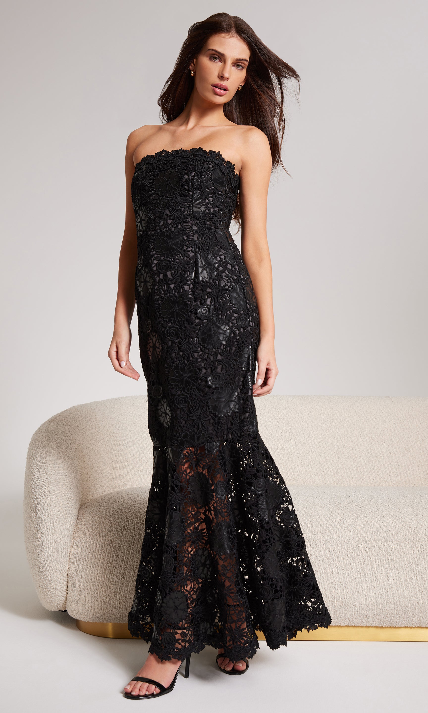 Woman wearing a black strapless leather+lace gown against a white background