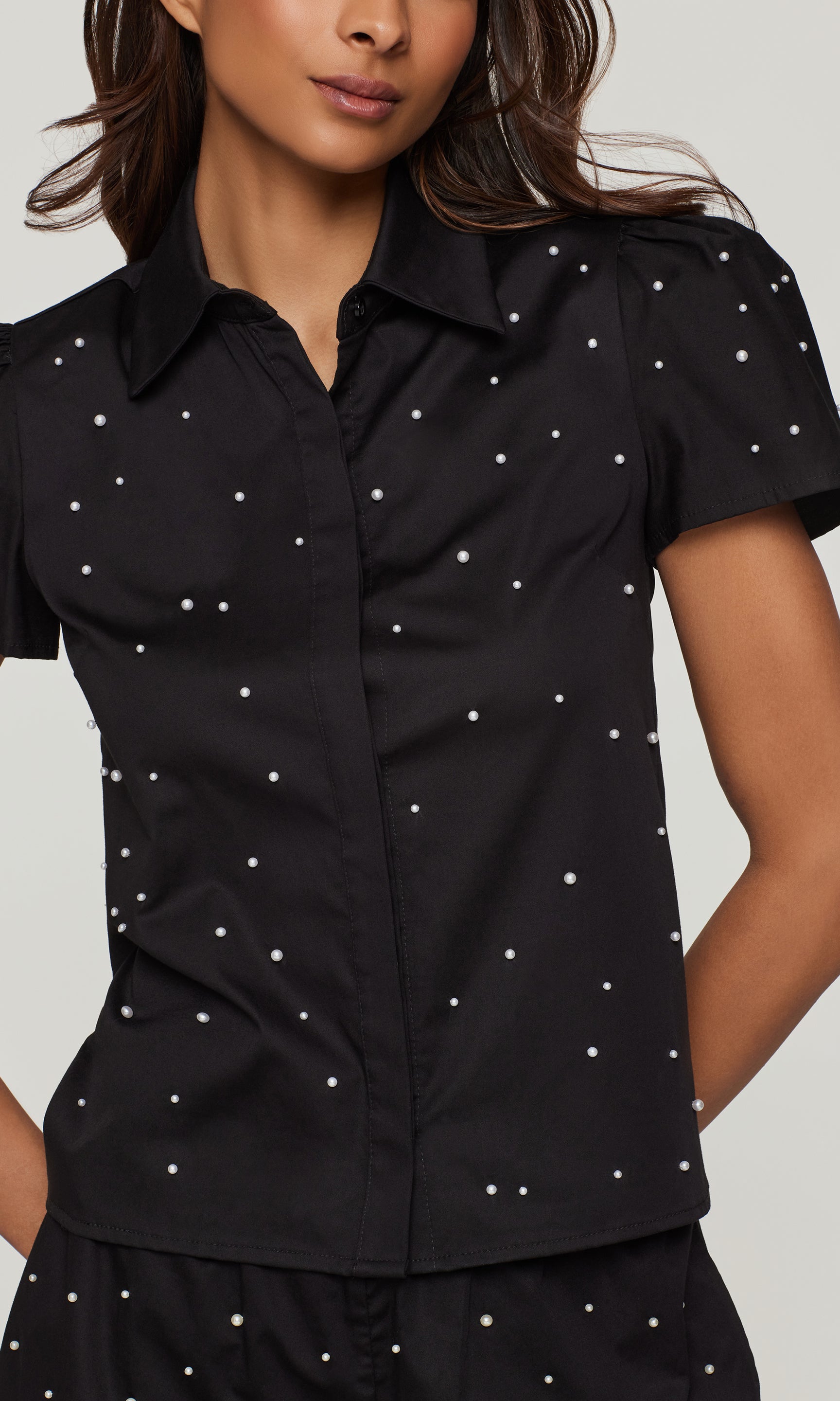 Black short-sleeve shirt with white pearls worn by a model on a neutral background