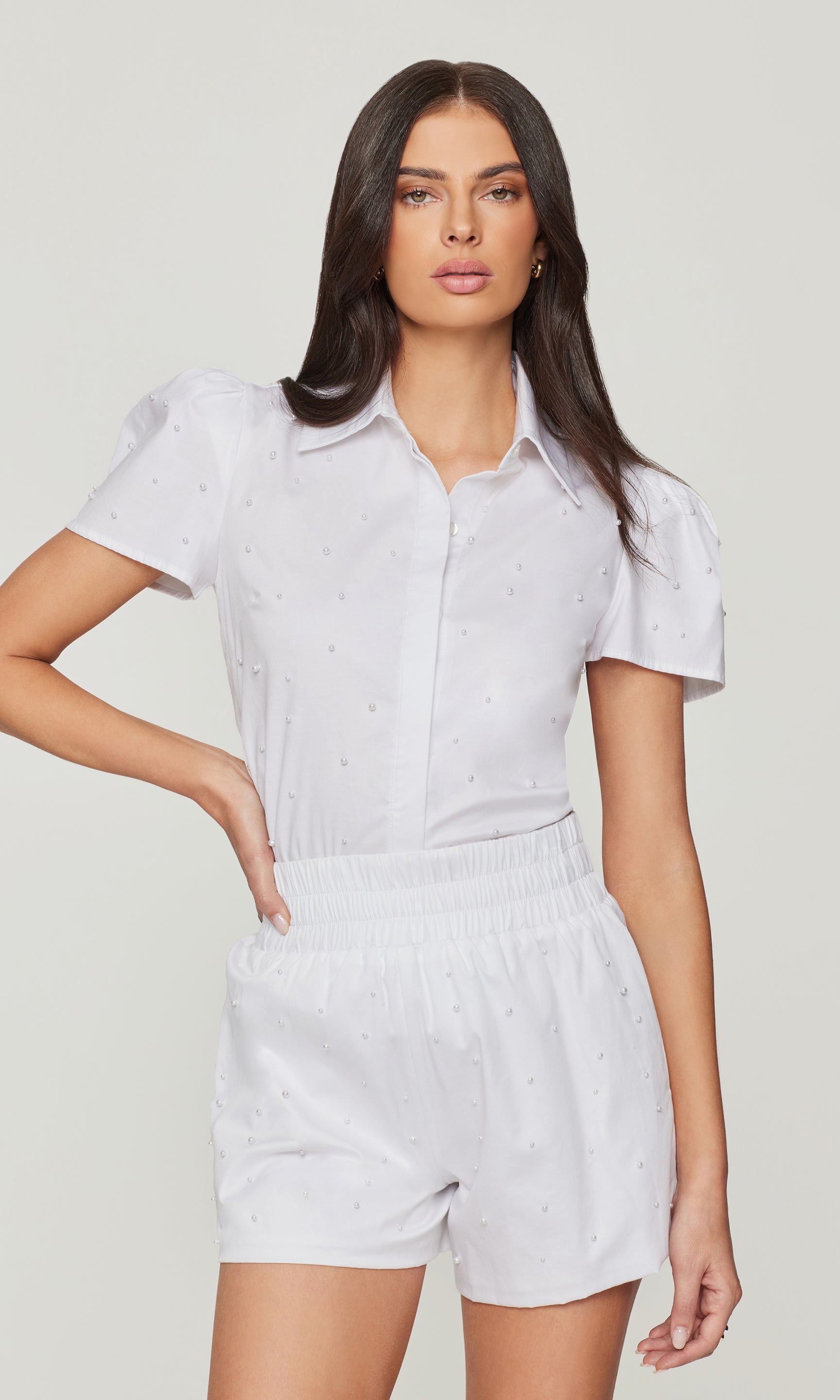 Woman wearing a white outfit with short sleeves and shorts on a plain background