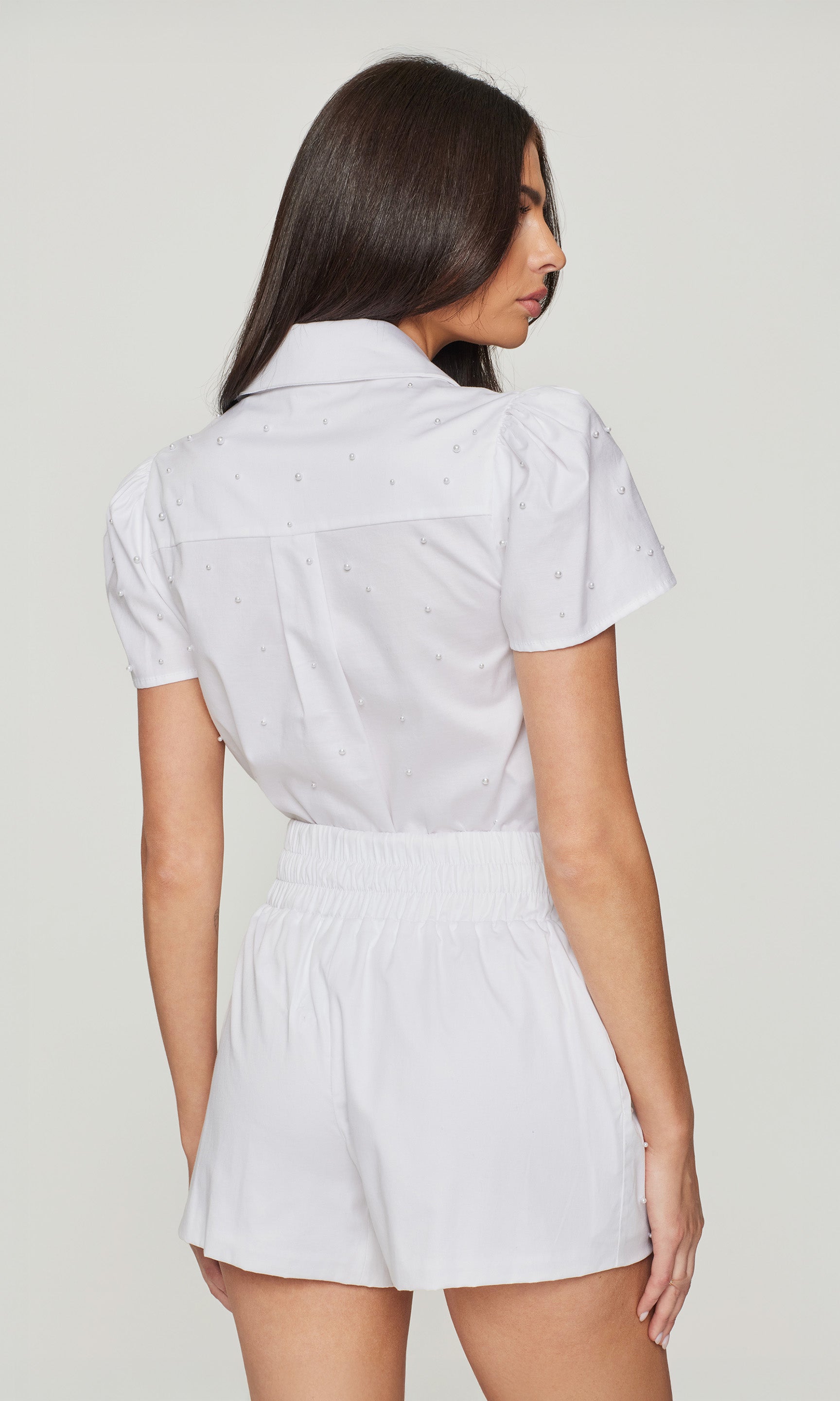 Woman wearing a white shirt and shorts set against a plain background