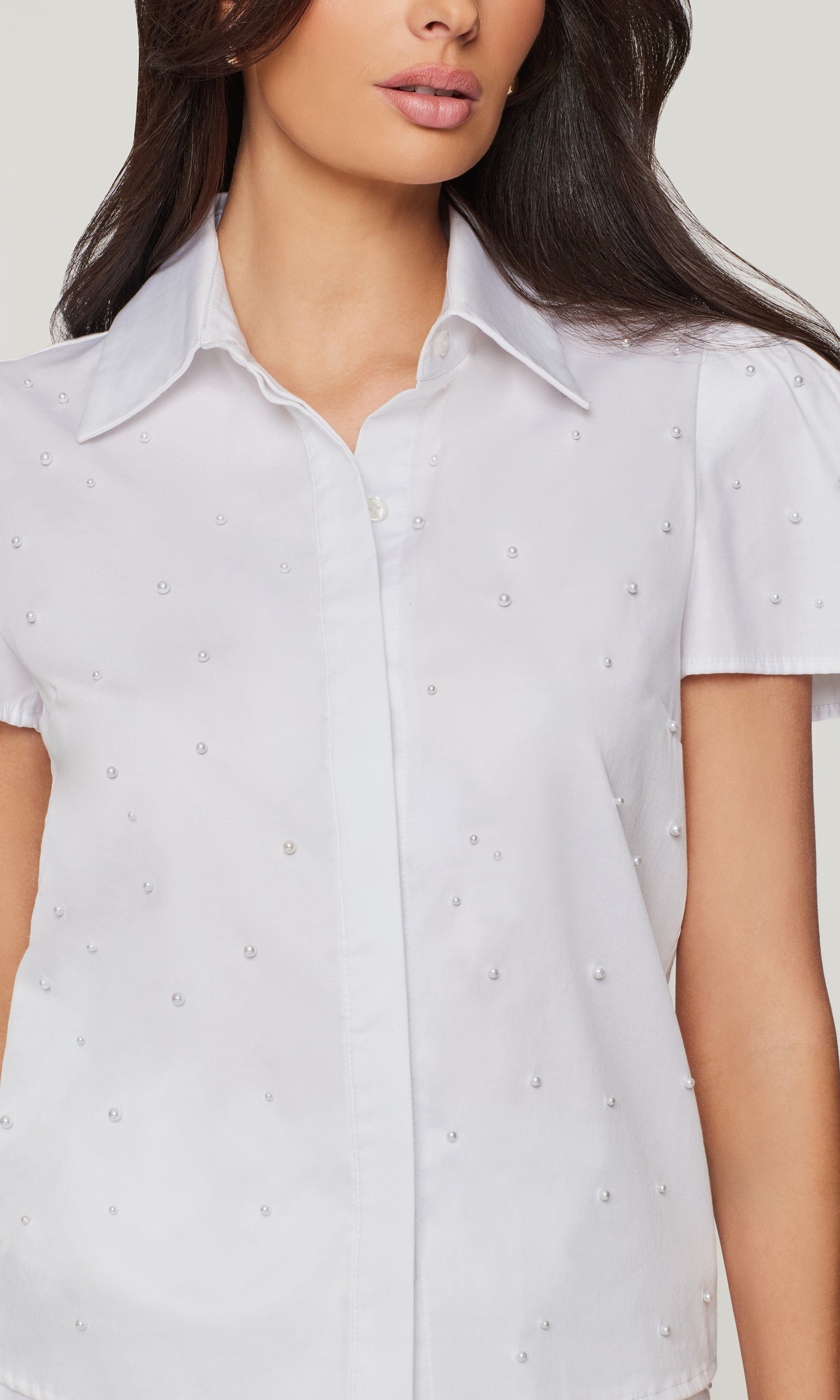 Woman wearing a white short-sleeve blouse with small pearl embellishments